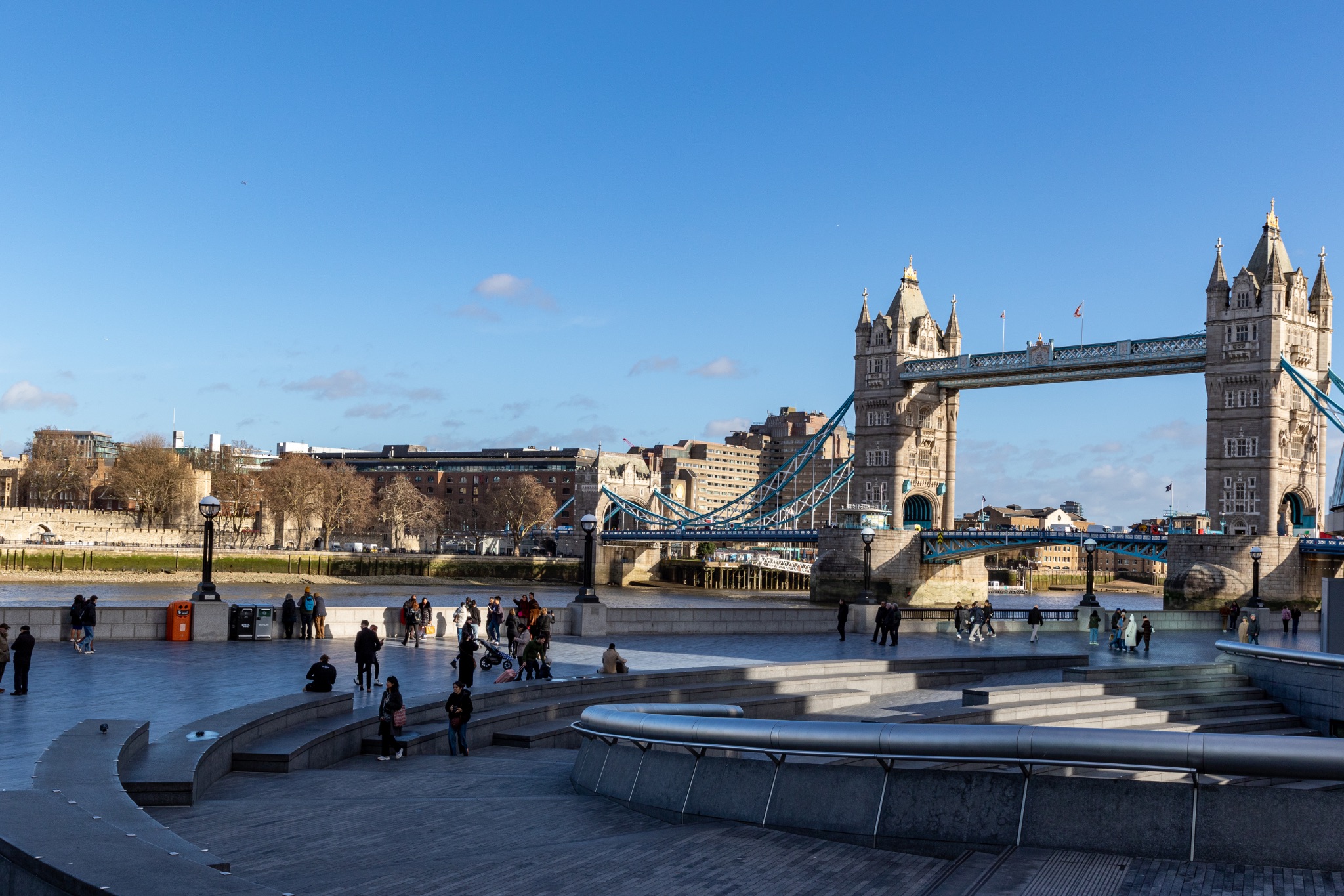 Sunny day at the iconic Tower Bridge in London with tourists enjoying the riverside view.
