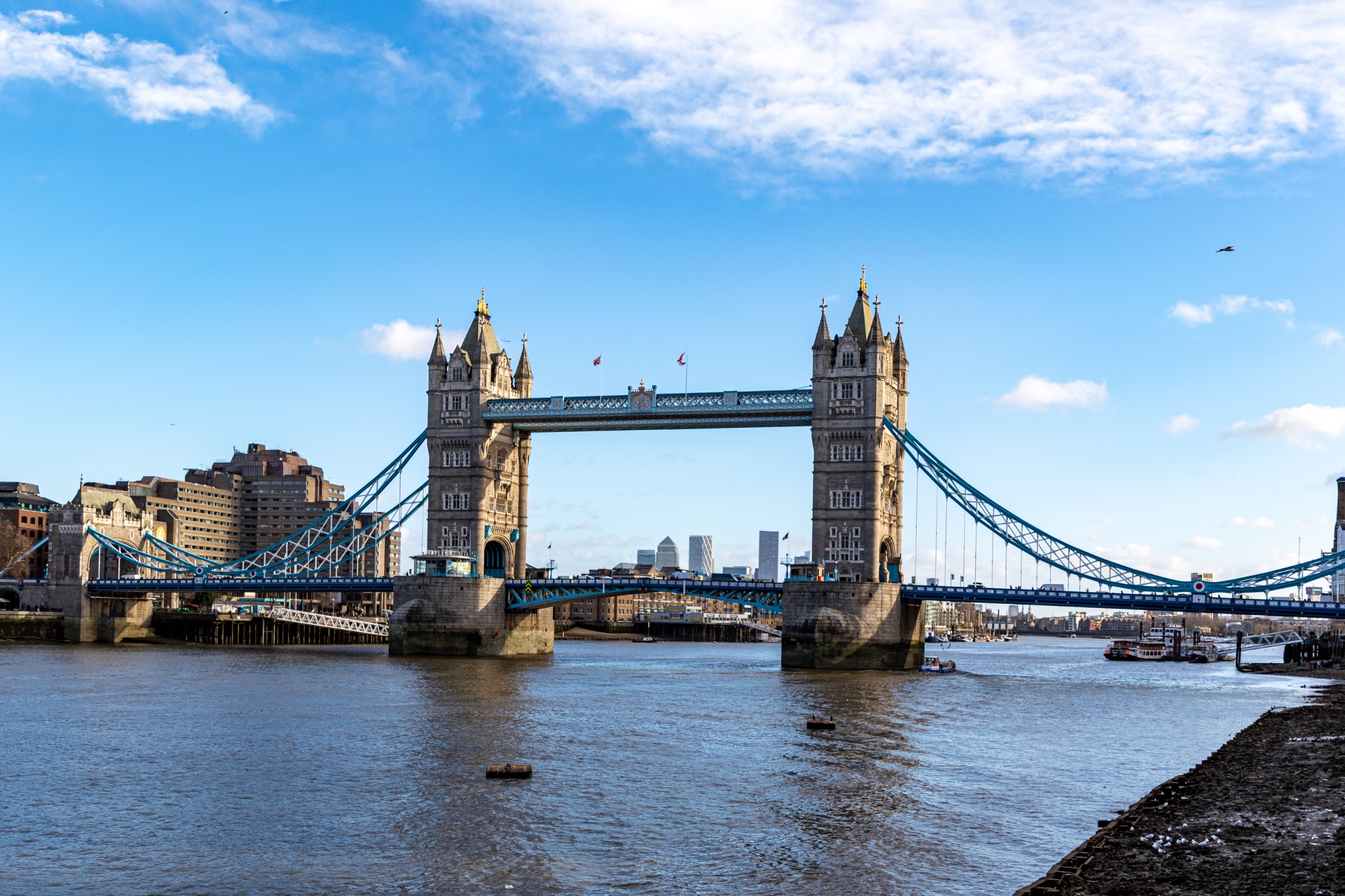 Sunny day view of the iconic Tower Bridge over the Thames in London, with clear blue skies and fluffy clouds.