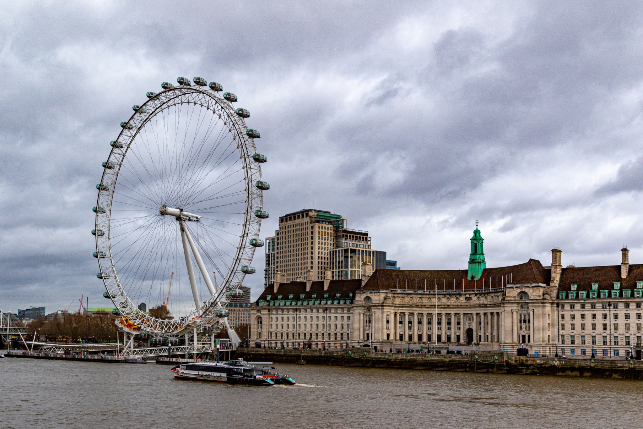 London skyline with the iconic London Eye Ferris wheel and River Thames on a cloudy day.