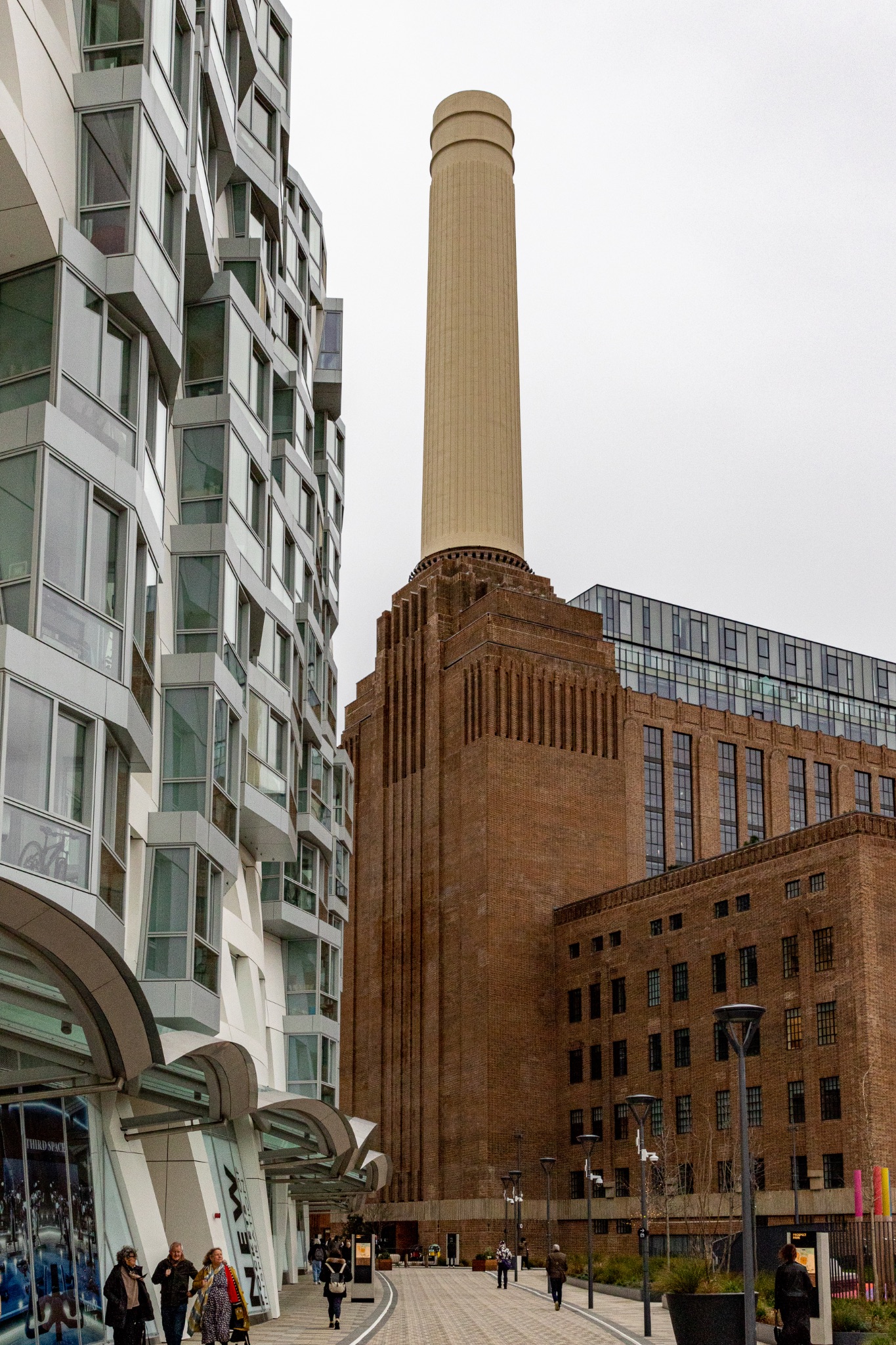 Modern residential building juxtaposed with a historic industrial chimney against a cloudy sky.