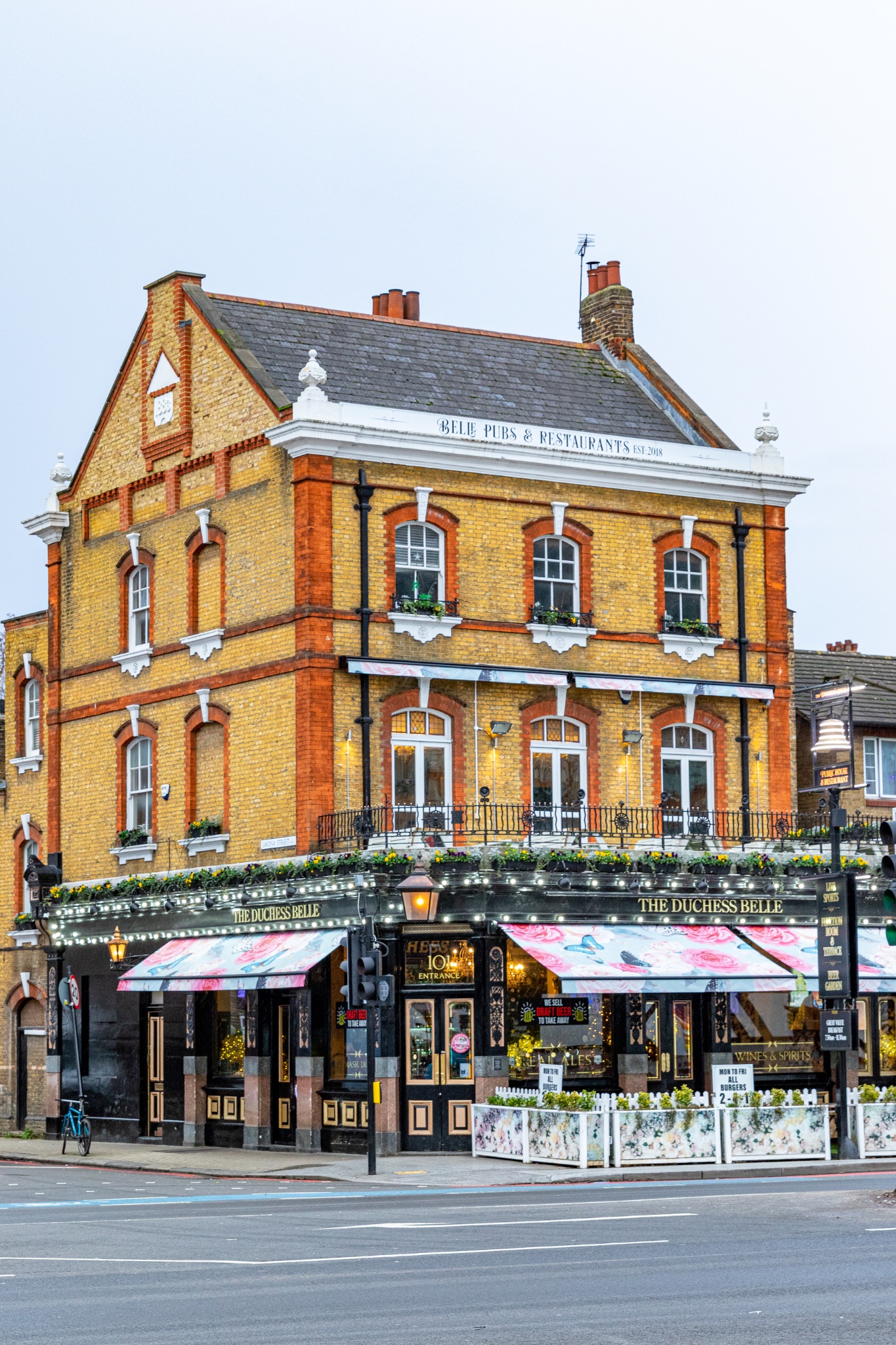 Traditional English pub with orange brick facade, decorated with greenery, in an urban setting.