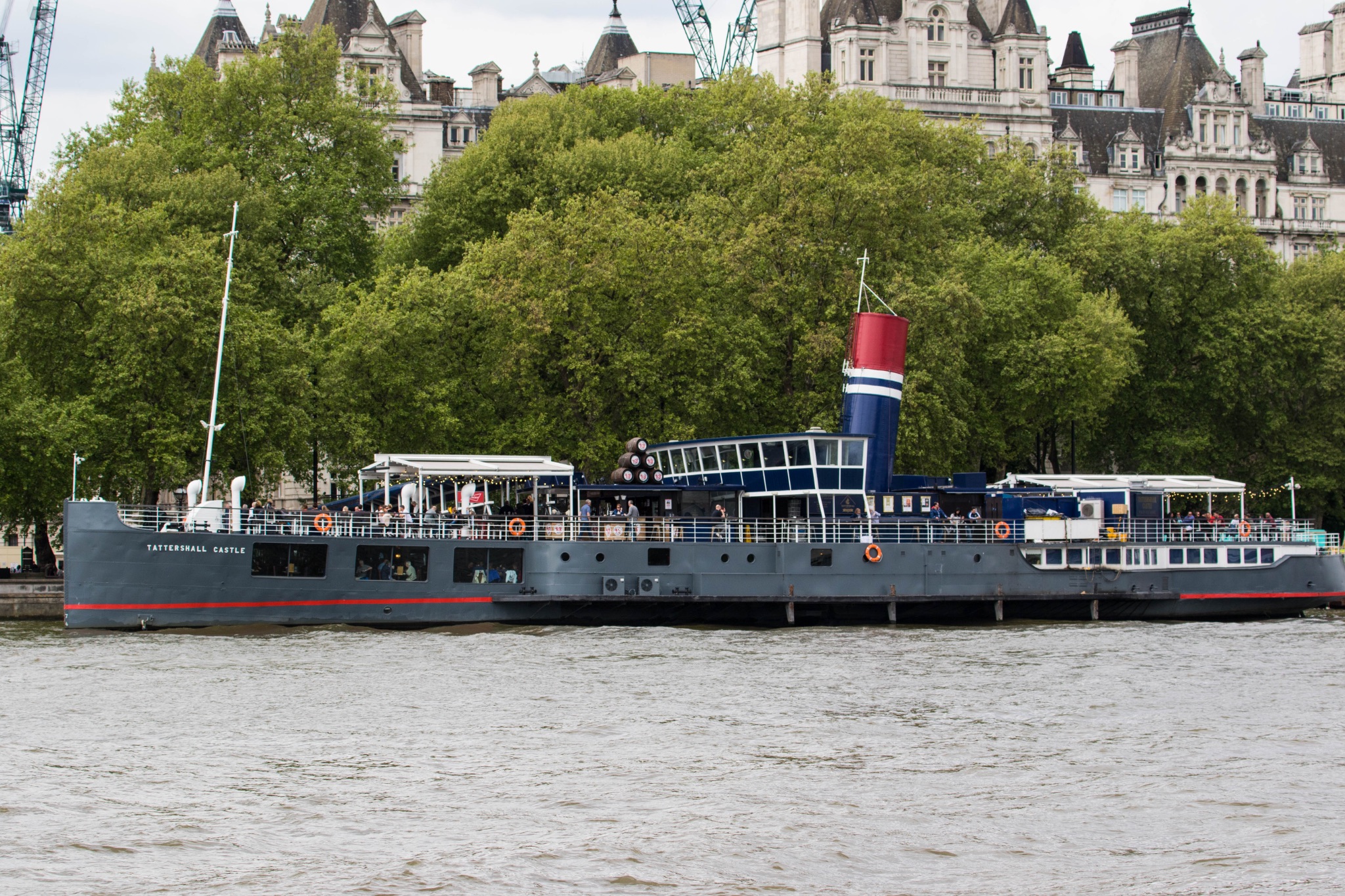 Tourist boat cruising on the Thames River with London's cityscape in the background.