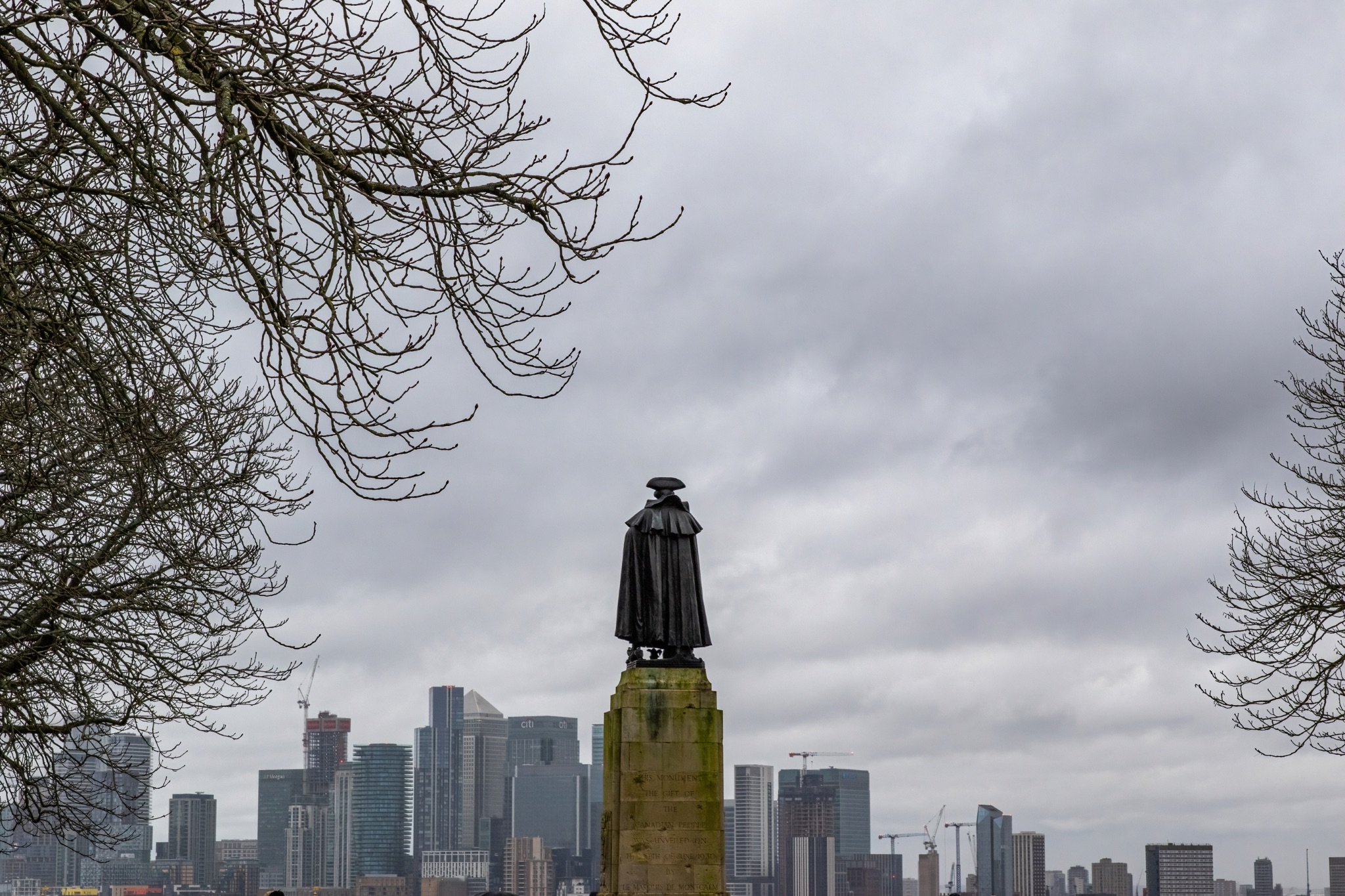 Statue silhouette against cloudy sky with modern city skyline in the background.