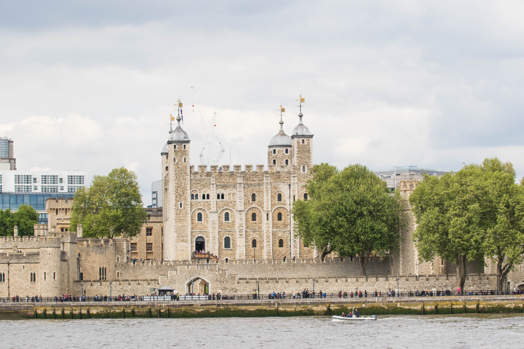 Historic Tower of London on the River Thames, iconic British landmark with cloudy sky.