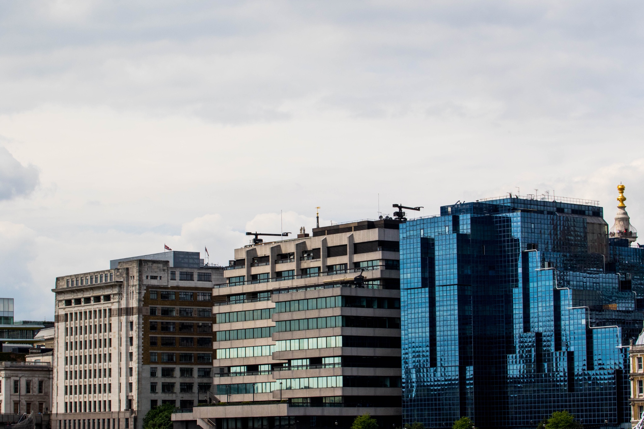 Contrast of modern blue glass skyscraper with traditional buildings against a cloudy sky.