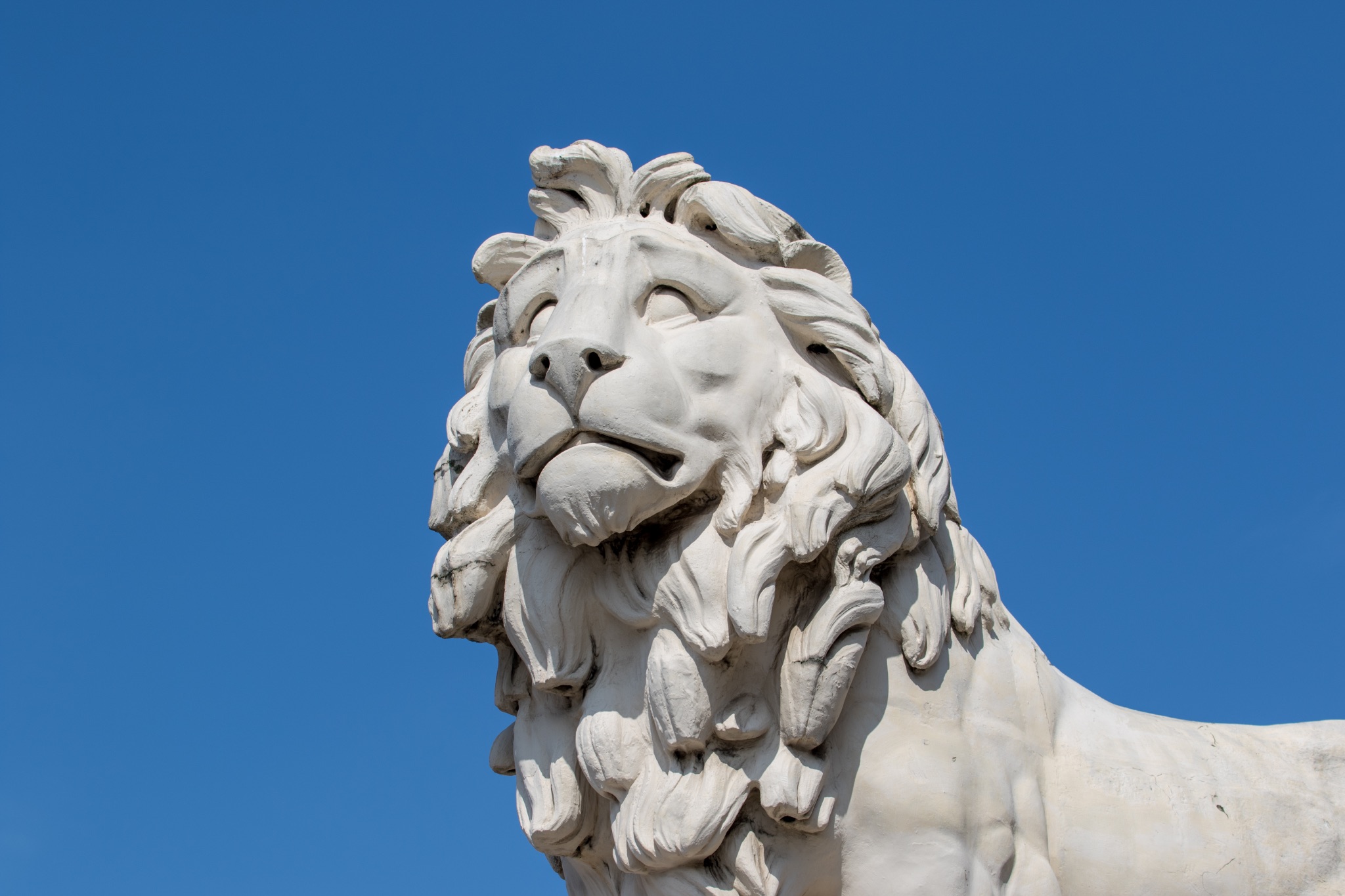 Marble lion statue against a clear blue sky, showcasing intricate details and craftsmanship.