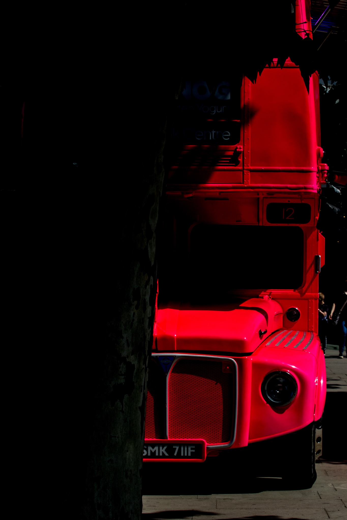 Red double-decker bus partially illuminated in contrasting shadows, iconic British transportation, side view with dark background.