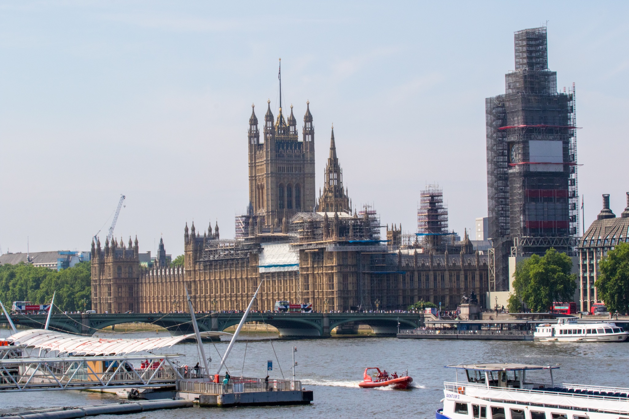 London skyline with the Houses of Parliament and Big Ben under scaffolding, Thames River with boats in the foreground.