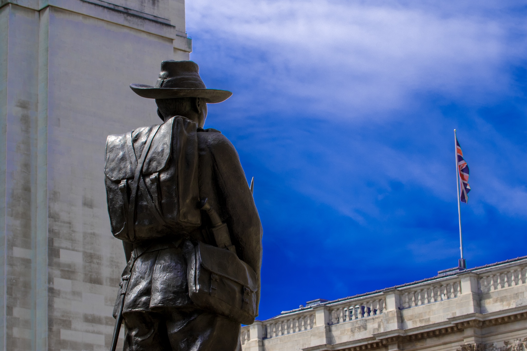 Silhouette of a soldier statue with a backpack against a blue sky with clouds and an American flag fluttering in the background.