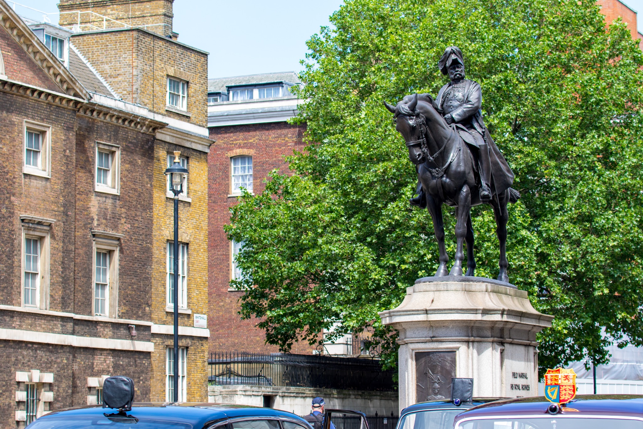 Equestrian statue in urban setting with historical buildings and green trees in the background, under a clear blue sky.