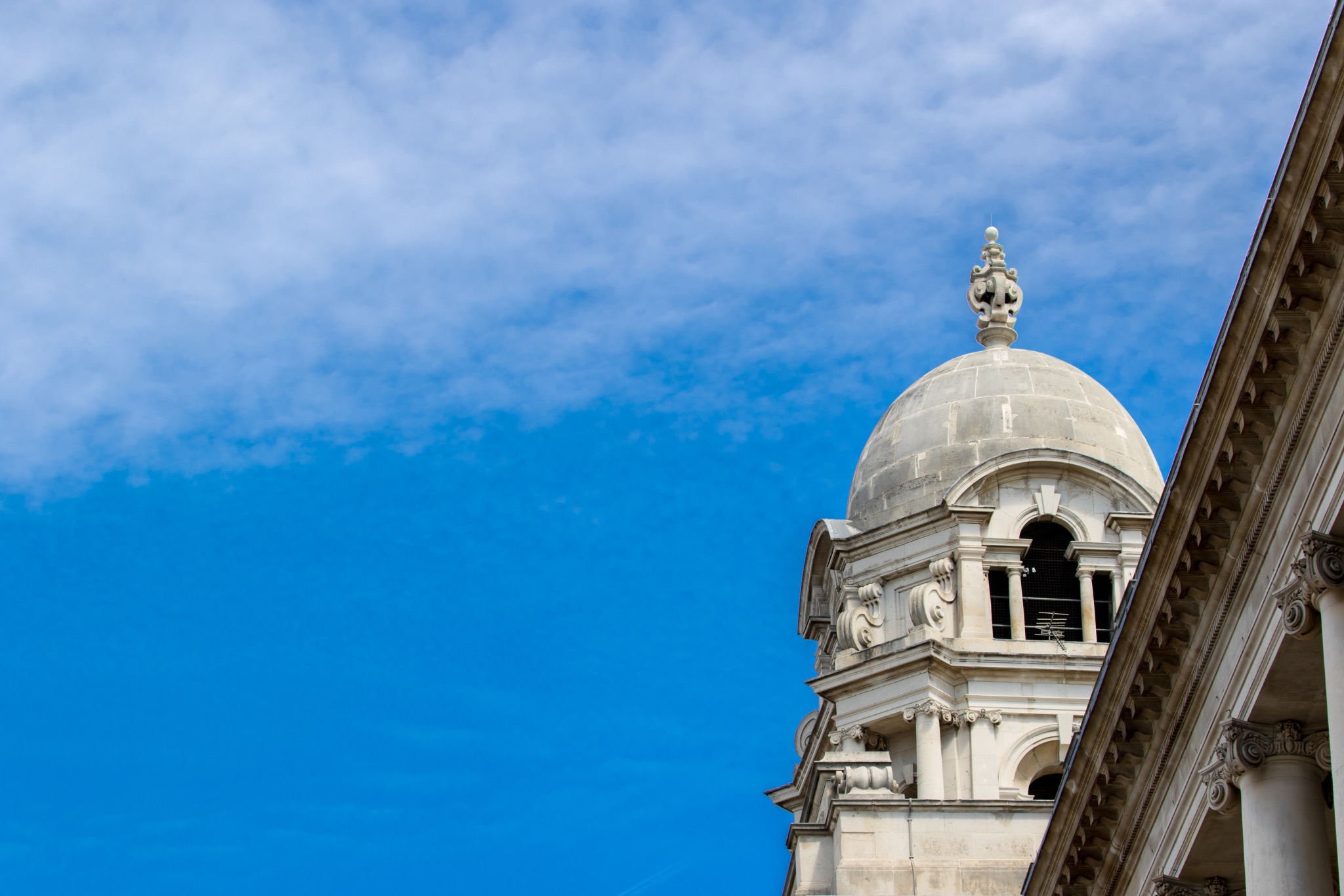 Classic architectural dome and facade against a blue sky with wispy clouds.