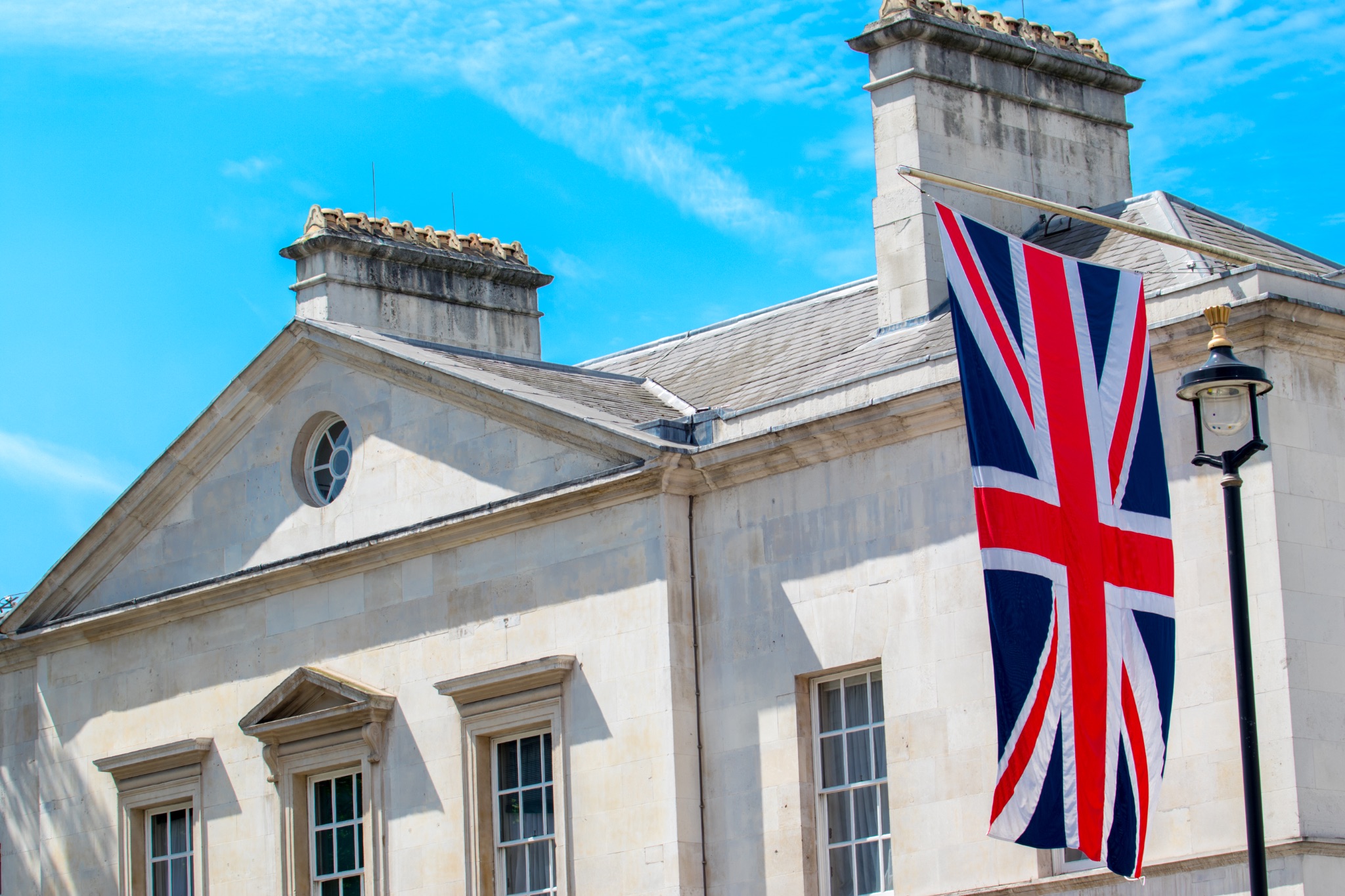 British flag hanging on a classic building with chimneys against a blue sky.