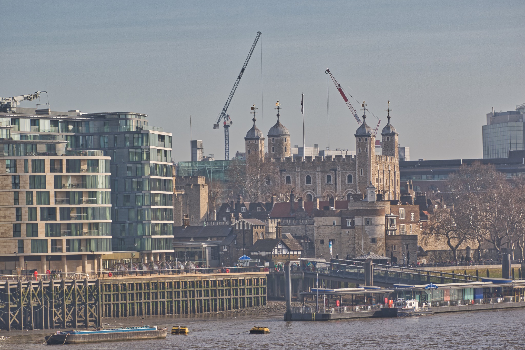 London skyline with the historic Tower of London and modern buildings, cranes in the background, over the River Thames.