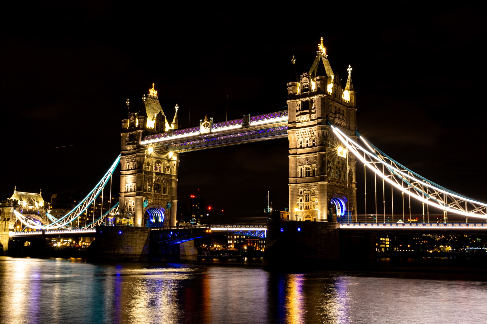 Night view of Tower Bridge in London with illuminated lights reflecting on the Thames River.