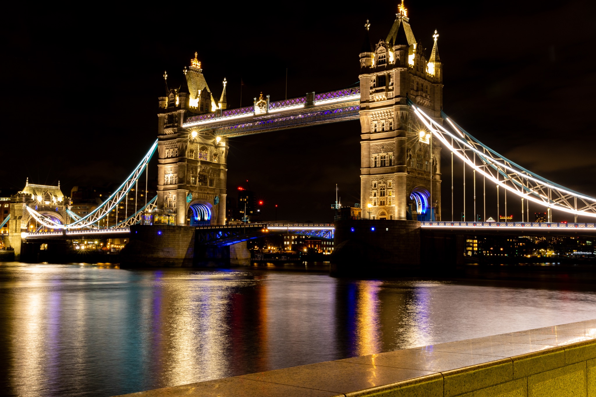 Illuminated Tower Bridge in London at night with reflections on the Thames River.