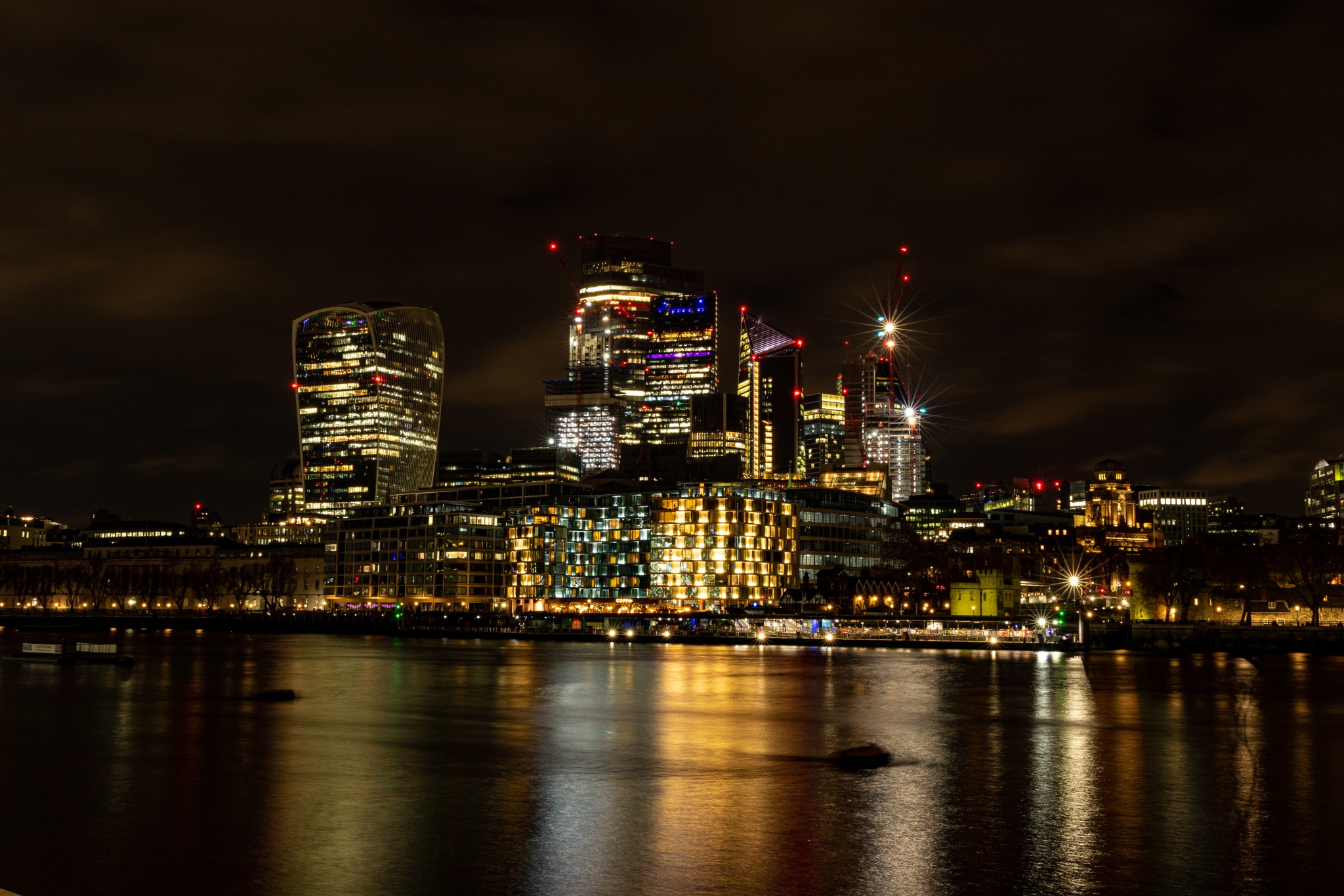 Nighttime cityscape with illuminated skyscrapers and reflections on water.