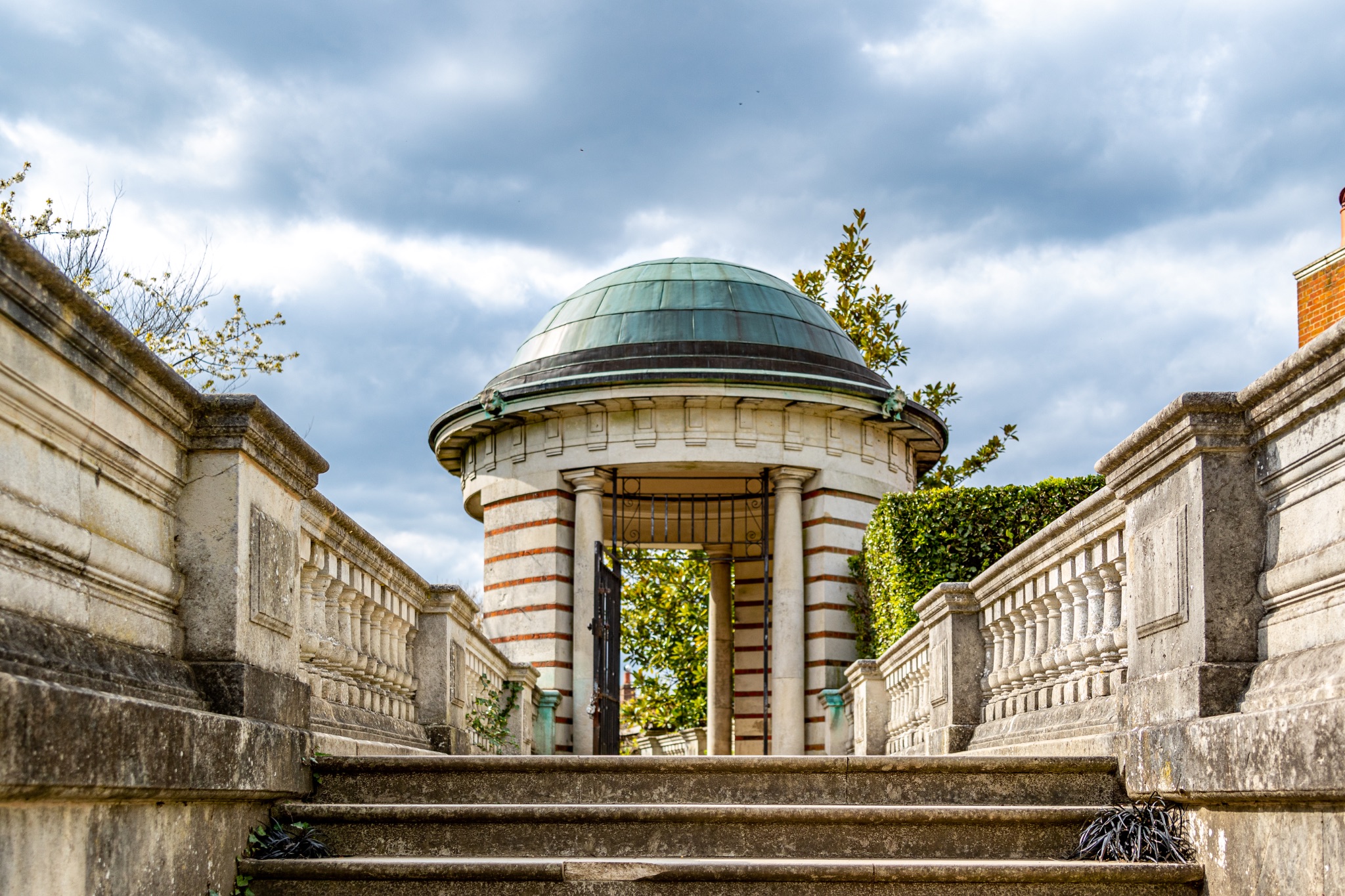 Classical stone gazebo with steps under a cloudy sky in The Hill Garden and Pergola in London.