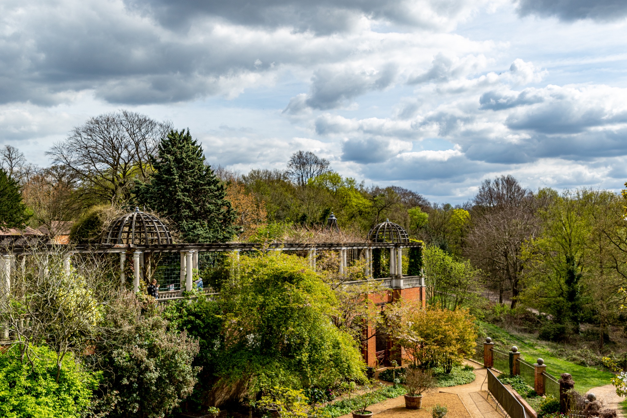Scenic view of a lush garden with overgrown ruins and dramatic clouds, showcasing nature's reclaim of historical architecture in The Hill Garden and Pergola in London.