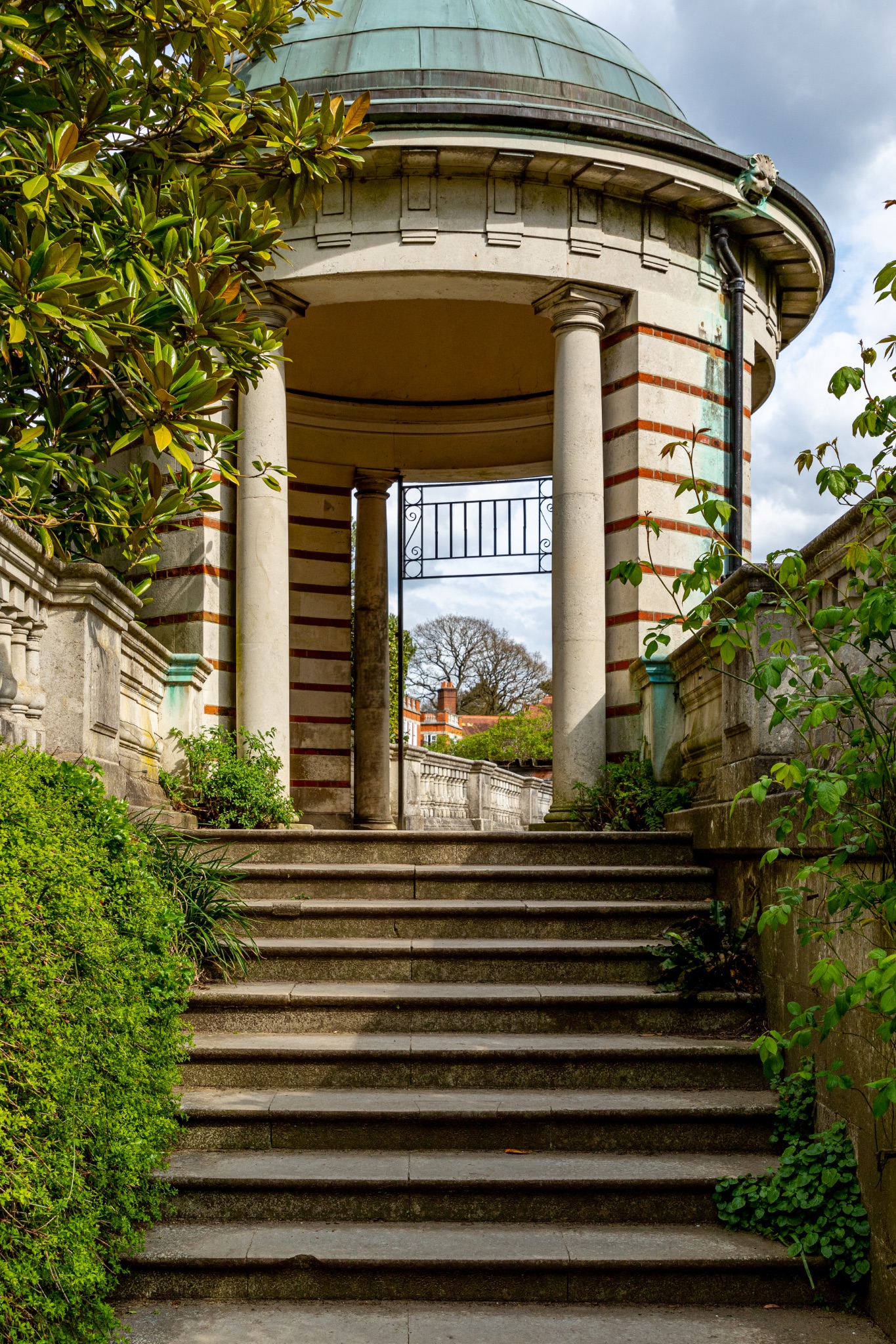 Classical stone gazebo with steps surrounded by lush greenery in a serene garden setting in The Hill Garden and Pergola in London.