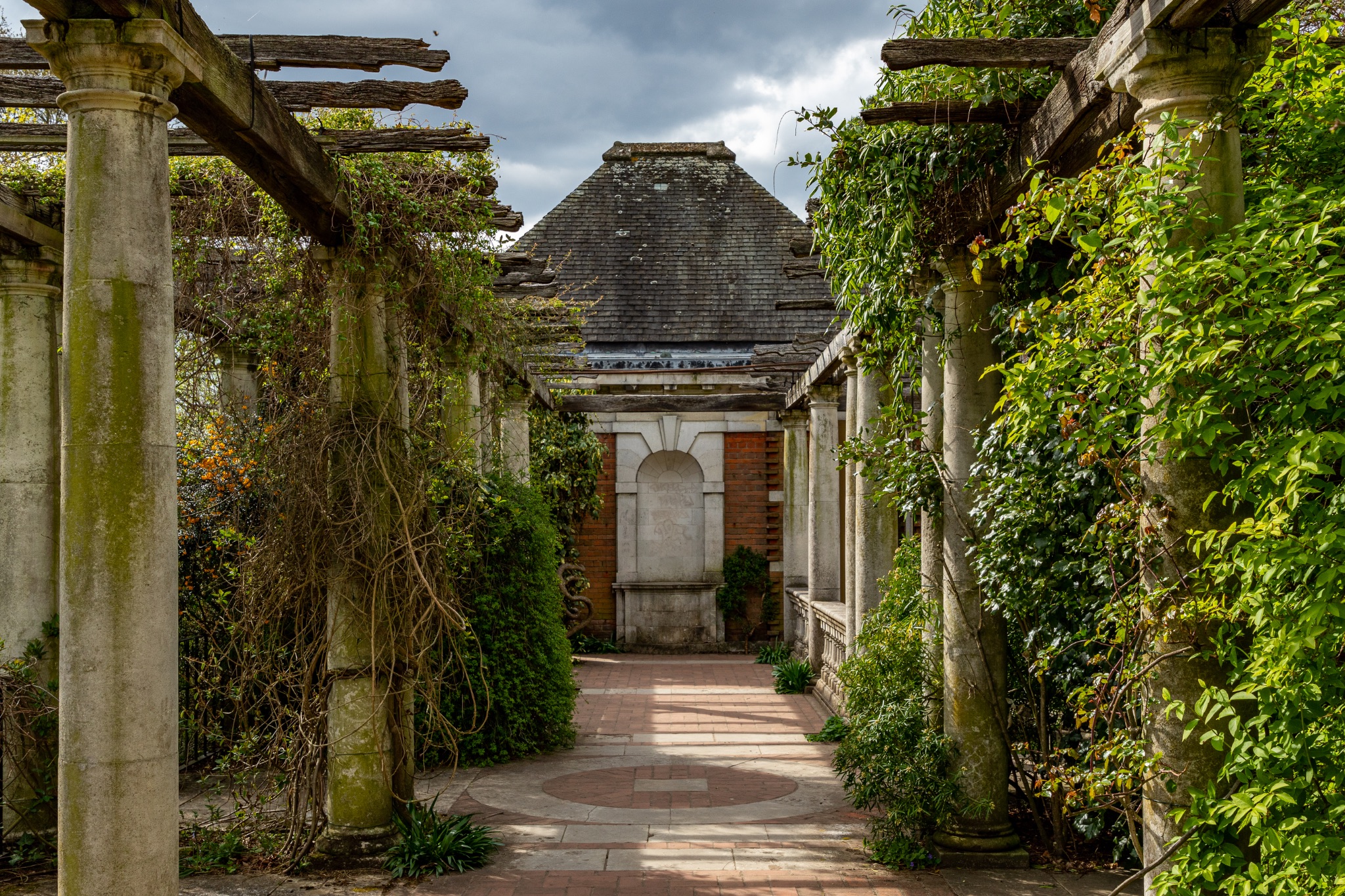 Pergola in a serene garden with climbing plants and a pathway leading to a classical building in The Hill Garden and Pergola in London.