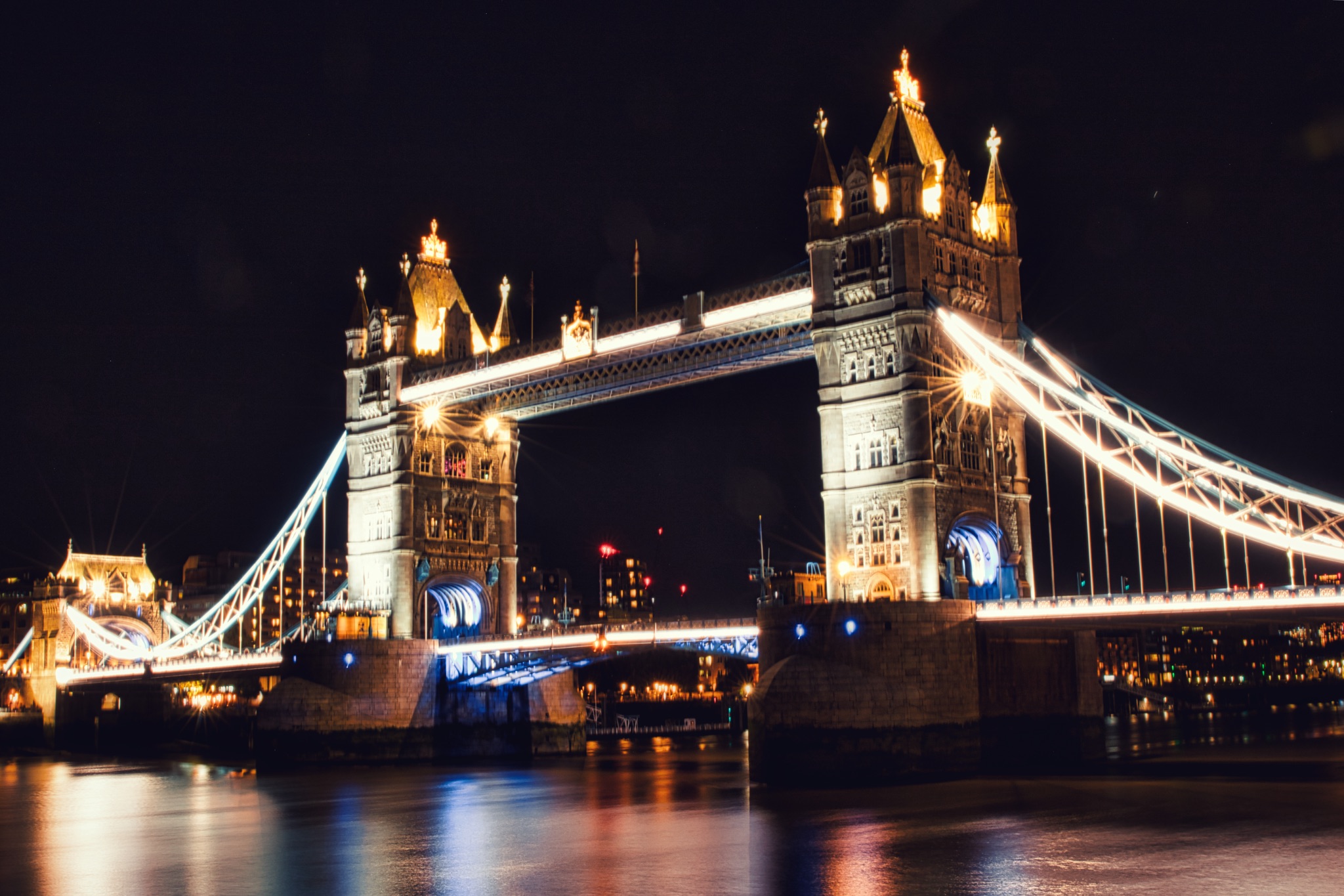 Night view of the illuminated Tower Bridge in London with reflections on the Thames River.