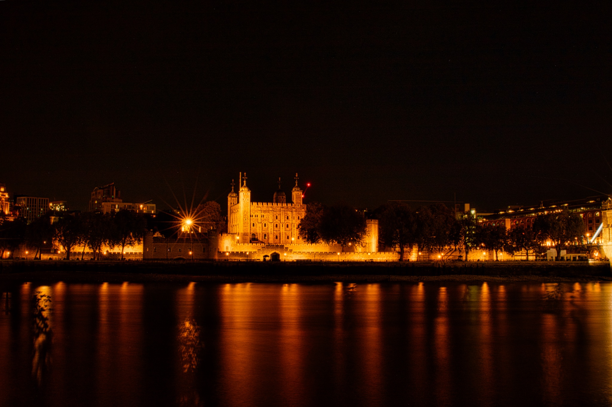 Night view of a lit-up historic building reflected in water, with city lights and dark sky.