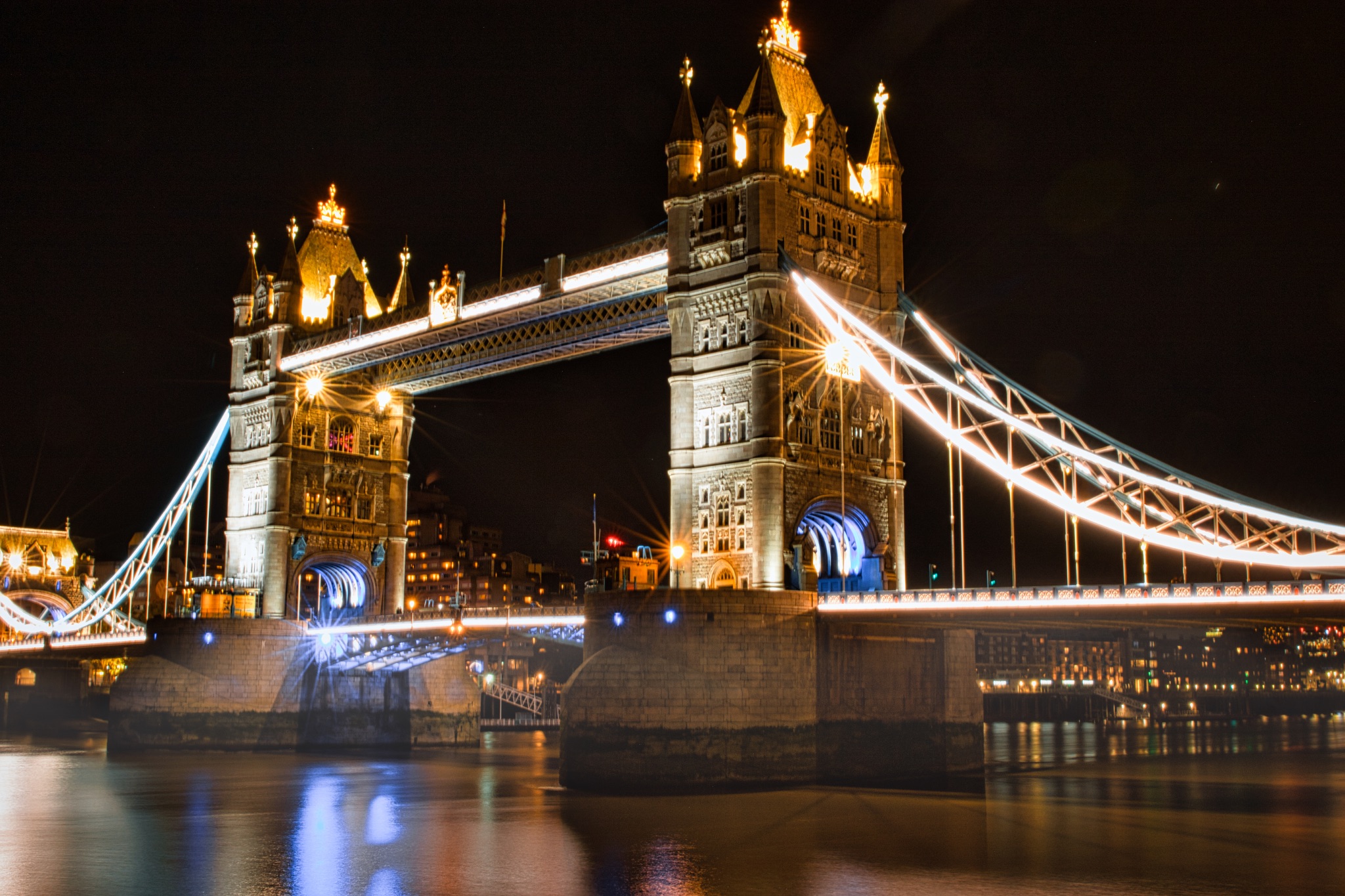 Night view of Tower Bridge in London with illuminated lights reflecting on the Thames River.