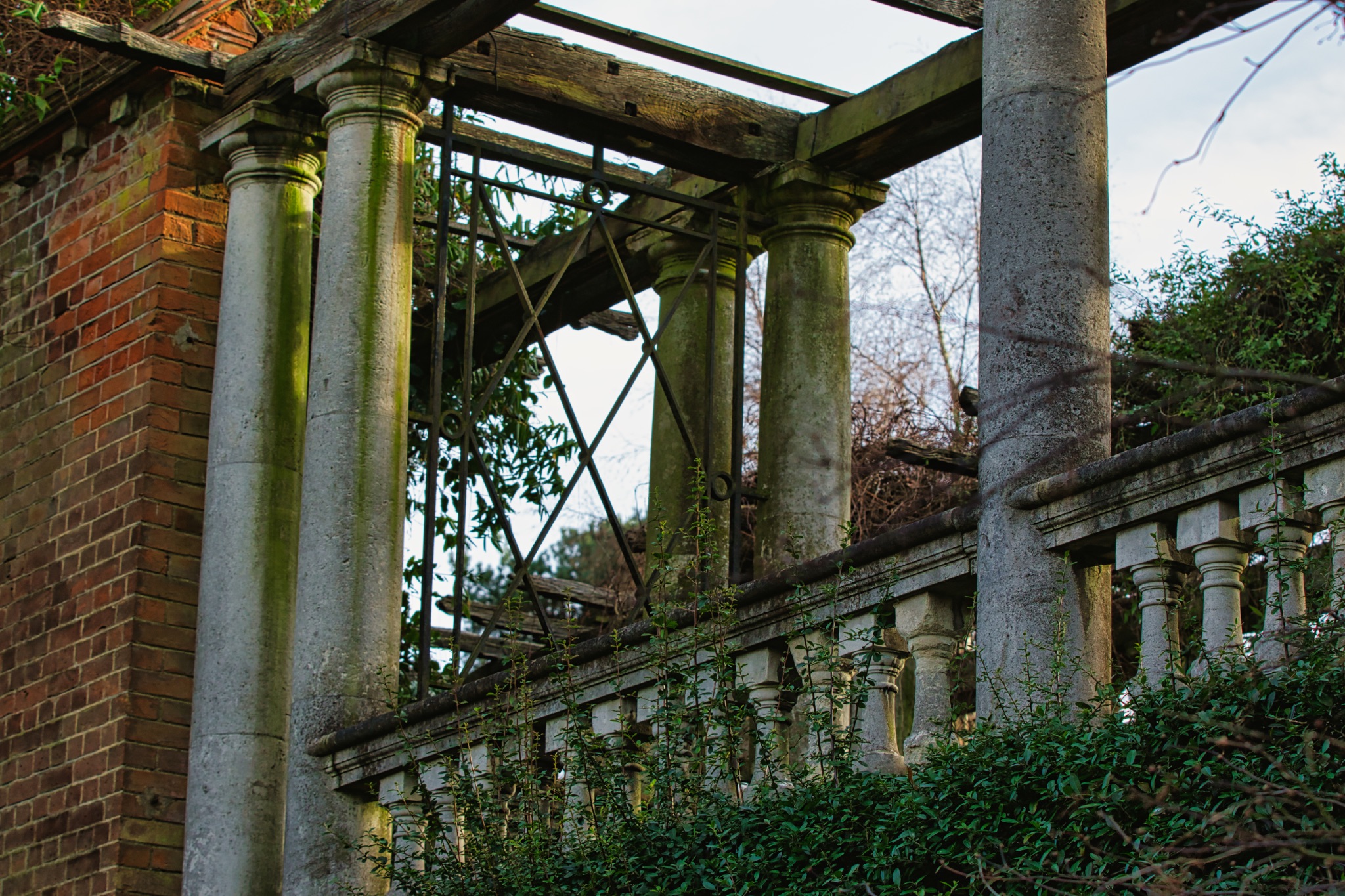Old weathered pillars and balustrade of a derelict building overgrown with ivy.