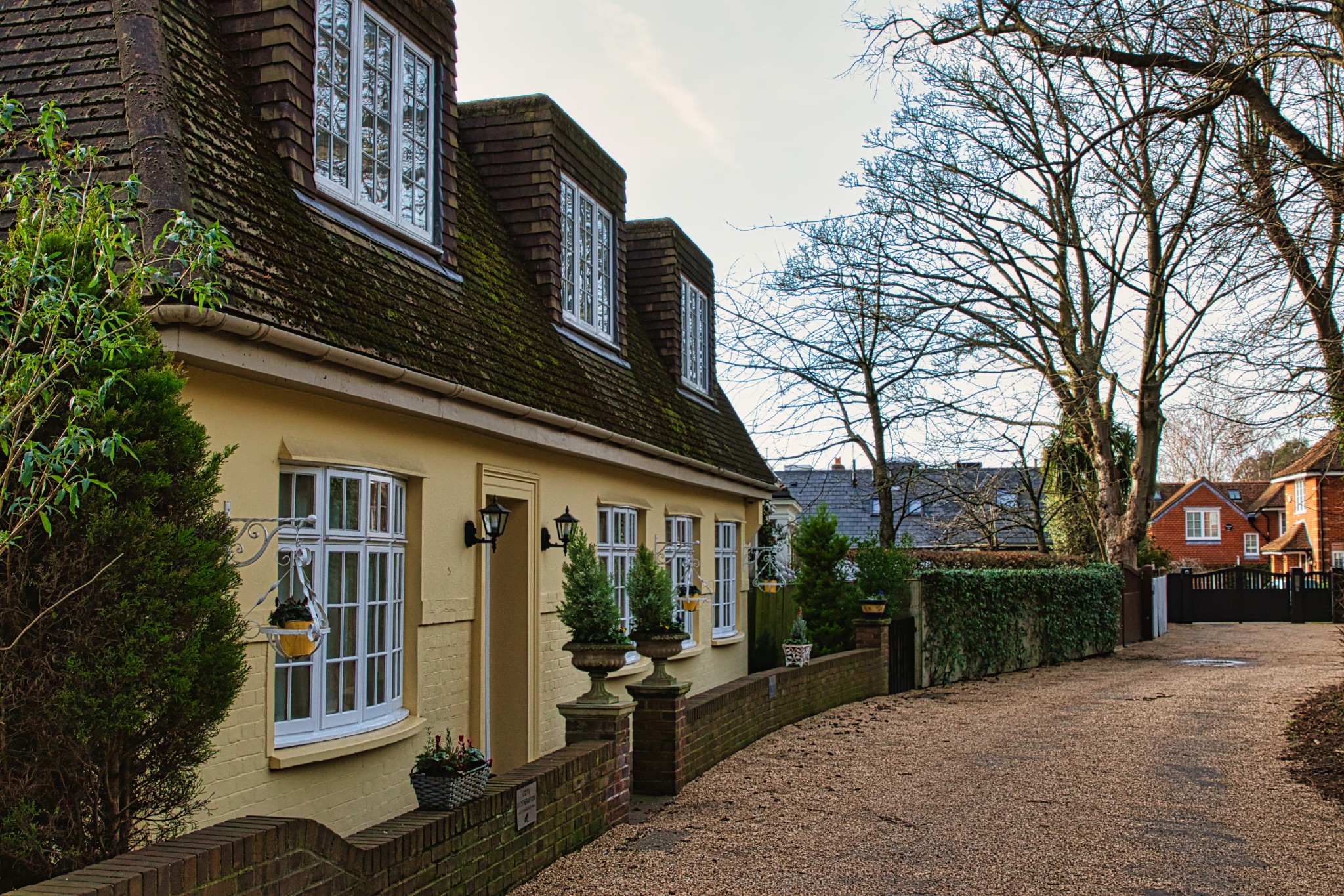 Traditional English cottage with yellow walls, white windows, and potted plants, set in a quaint village street.