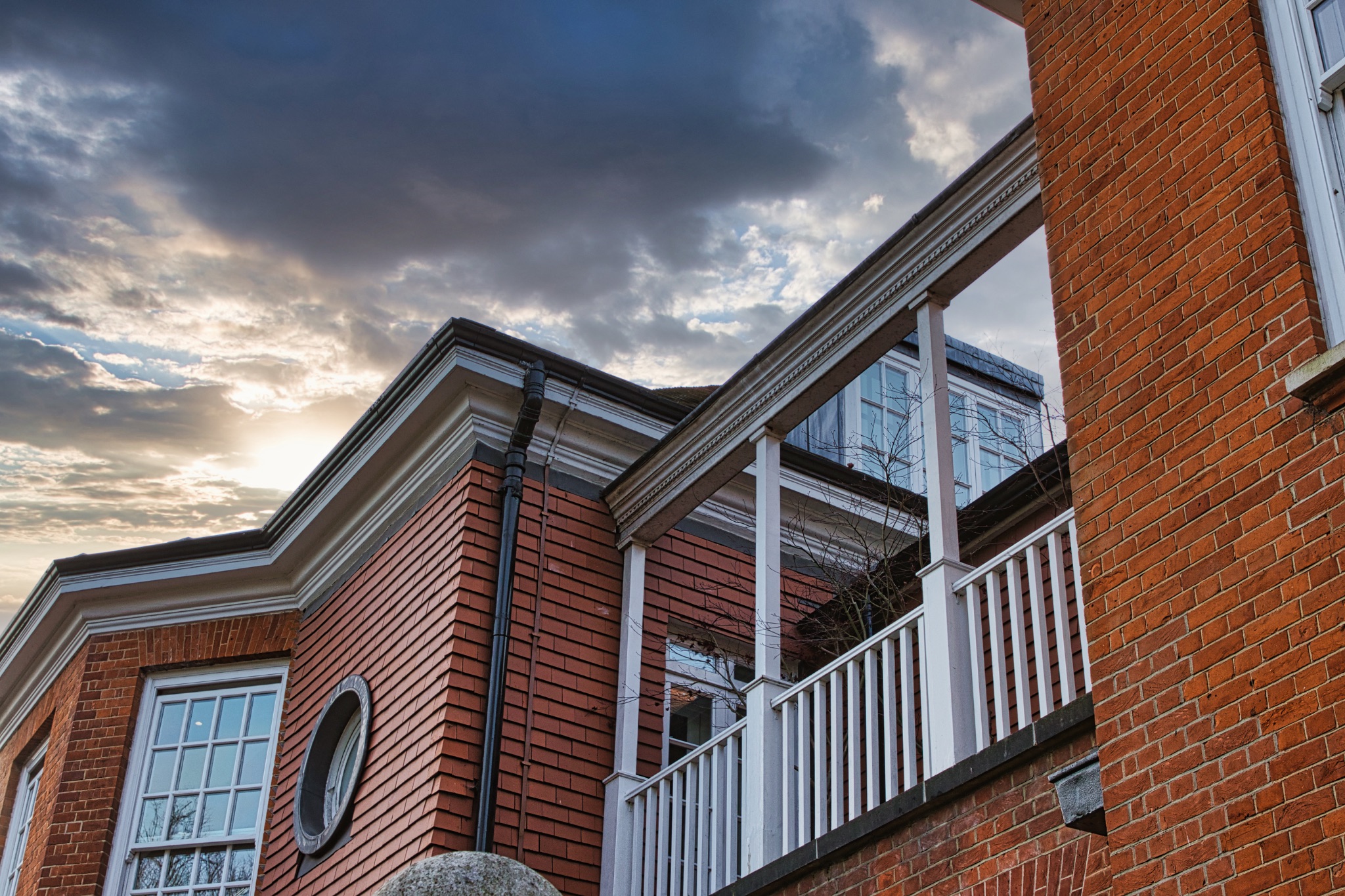 Traditional brick house with white balcony under a dramatic sky at dusk.