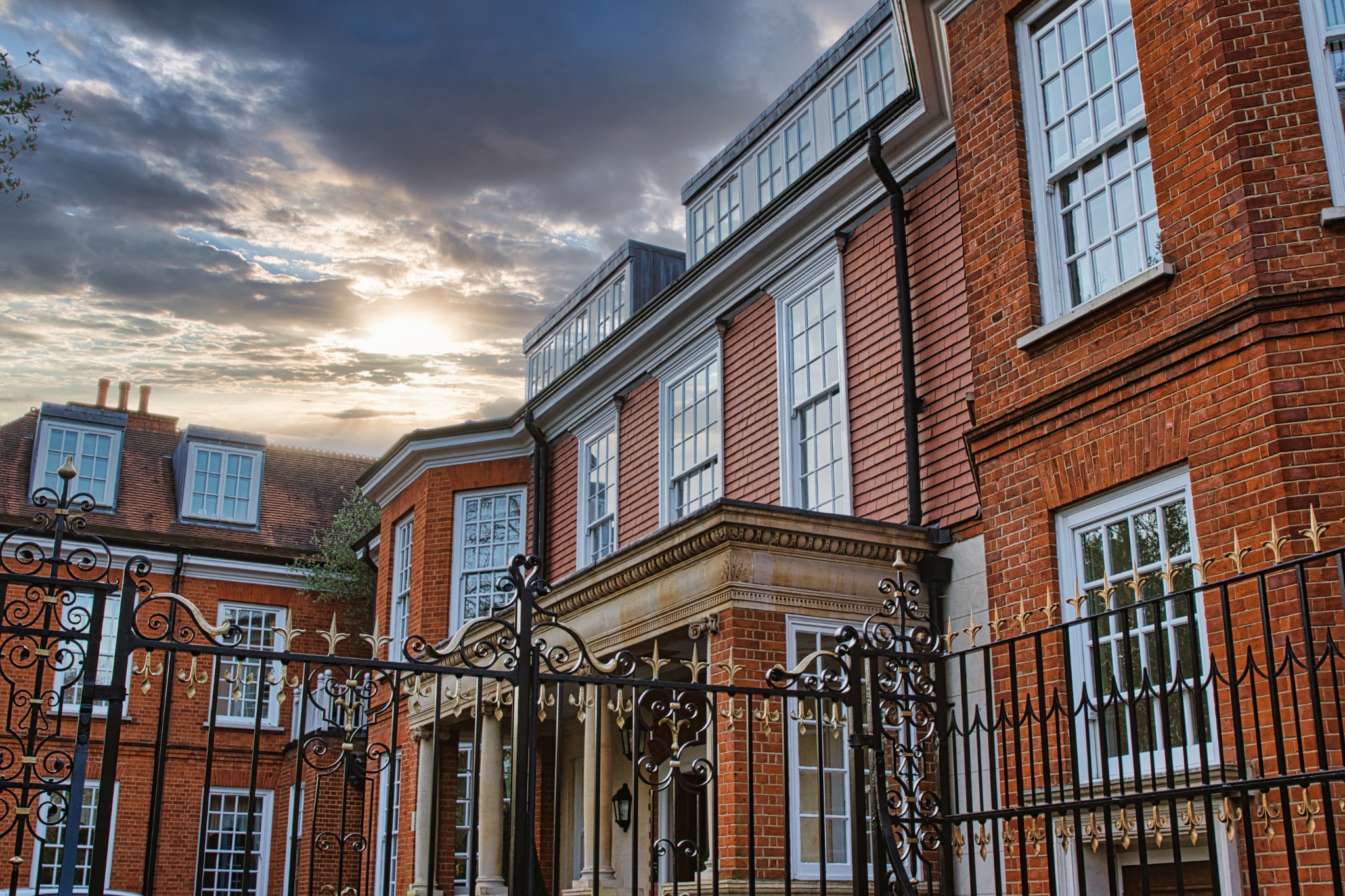 Traditional brick building with large windows and ornate iron gate at sunset, showcasing architectural details and warm sky.