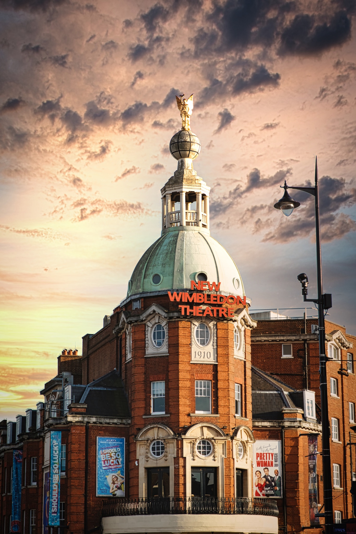Dramatic sky over Wimbledon Theatre with golden sunset light illuminating the building's facade and dome.