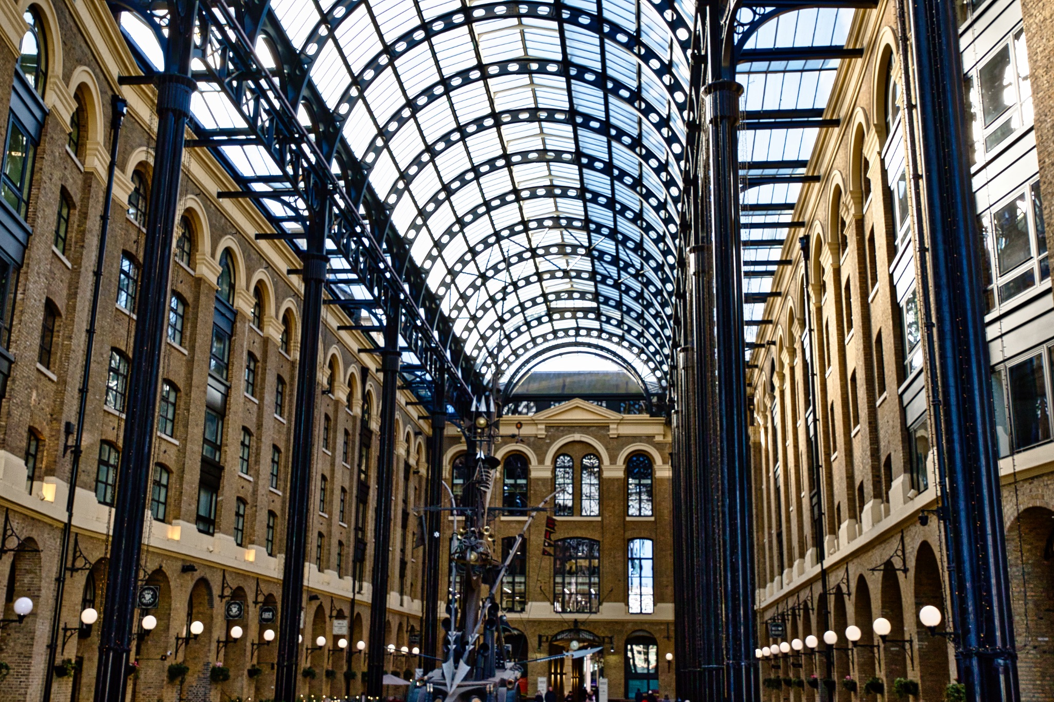Glass-Roofed Arcade with Central Sculpture and Brick Buildings in London, UK.