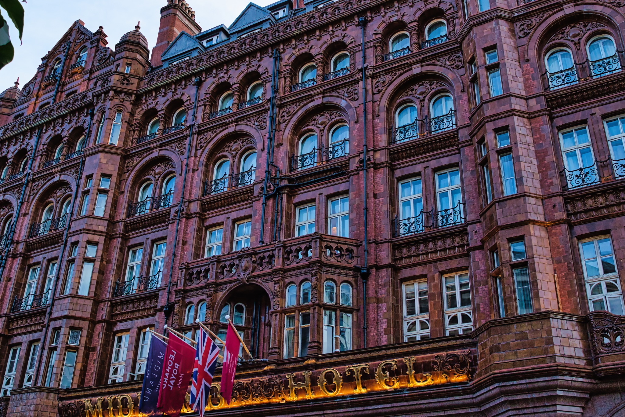 Facade of a grand Victorian building with intricate architecture and warm lighting at dusk in Manchester, England.