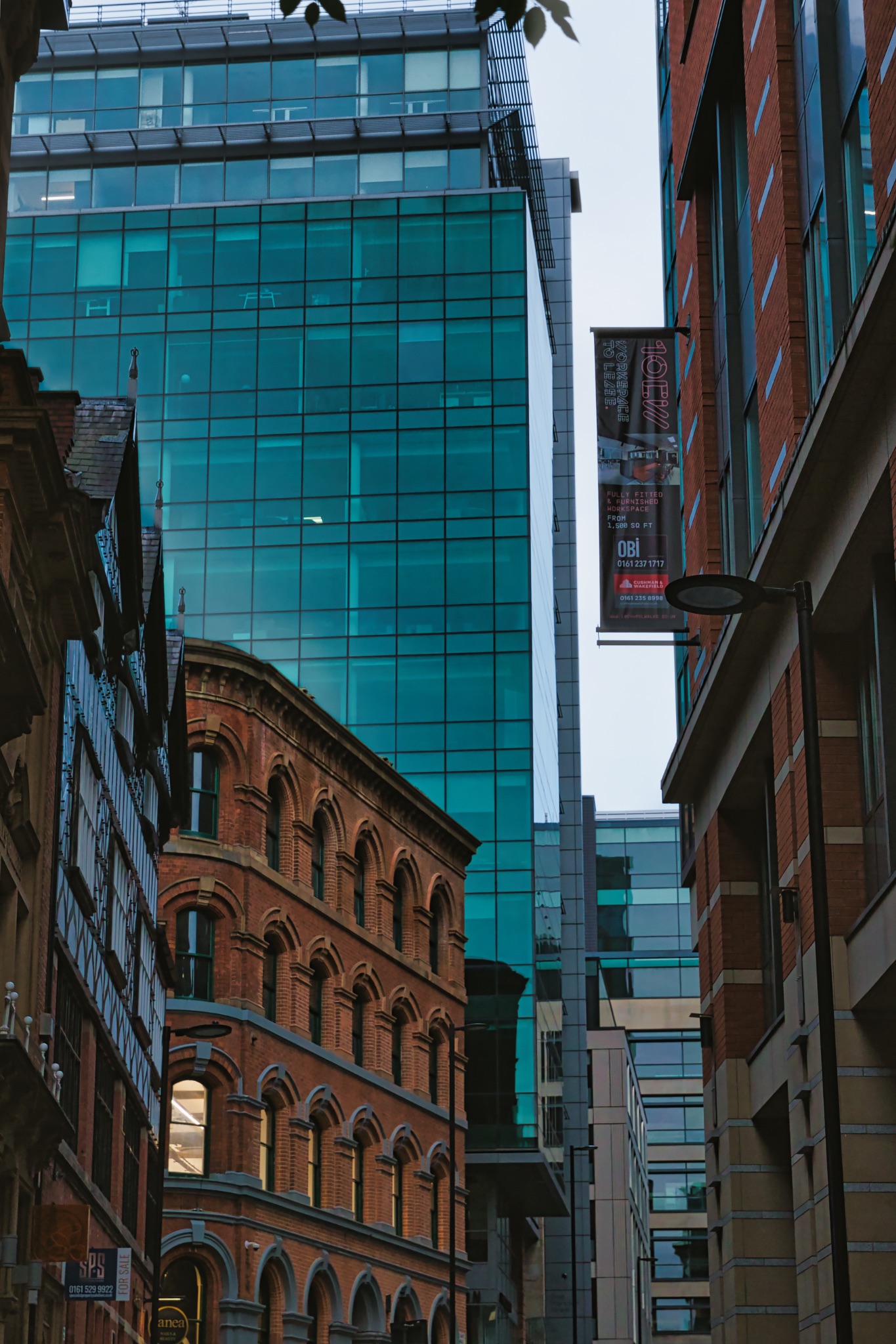 Urban cityscape with historic architecture contrasting against modern skyscrapers under a dusk sky in Manchester, England.