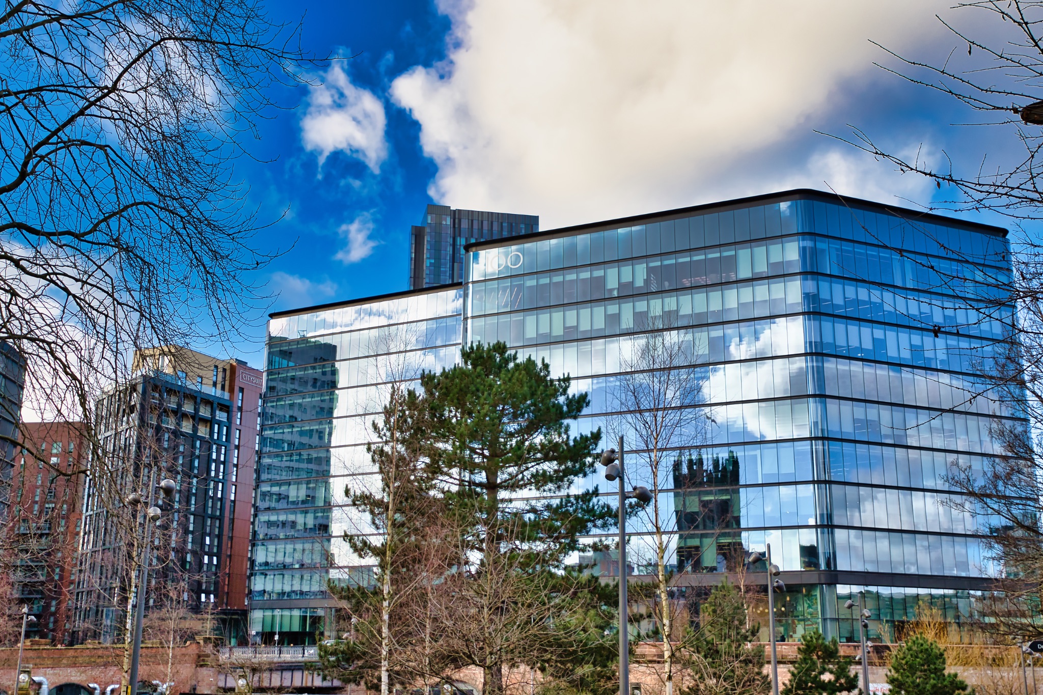 Modern Glass Building Reflection with Surrounding Structures in Manchester, UK.