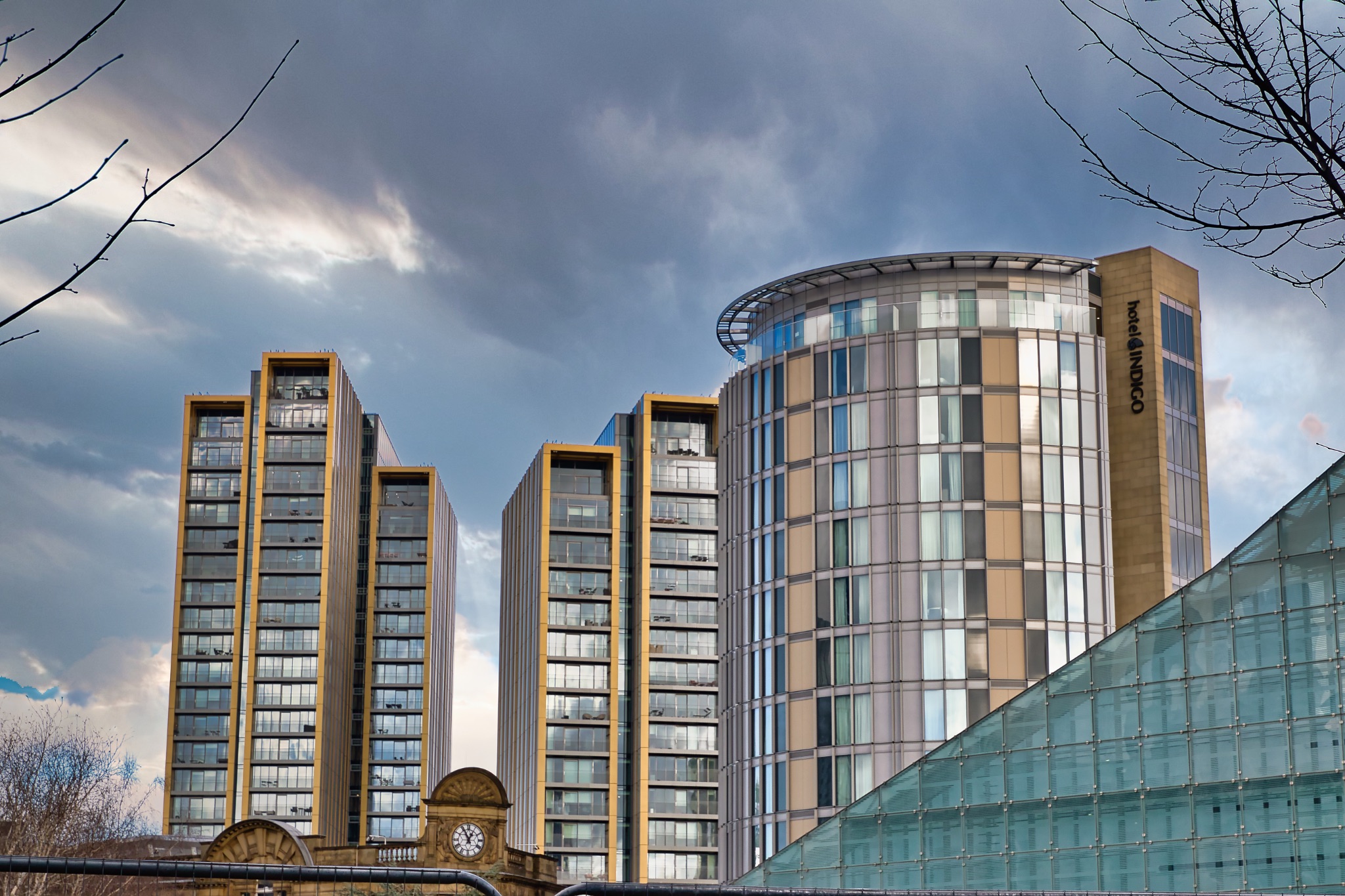Three High-Rise Buildings and Partial Glass Structure Under Cloudy Sky in Manchester, UK.