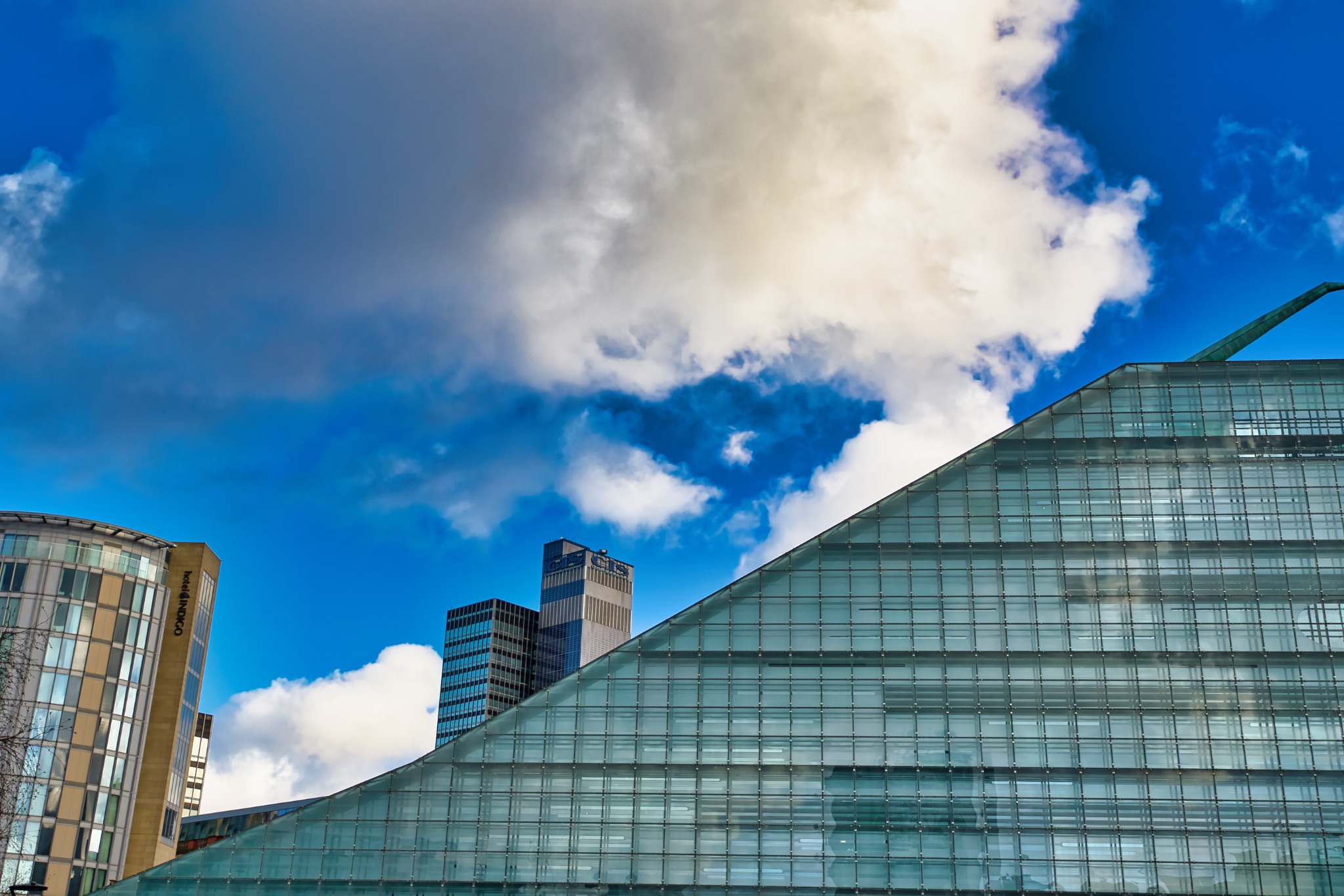 Modern Glass Structure and Adjacent Buildings Under a Partly Cloudy Sky in Manchester, UK.