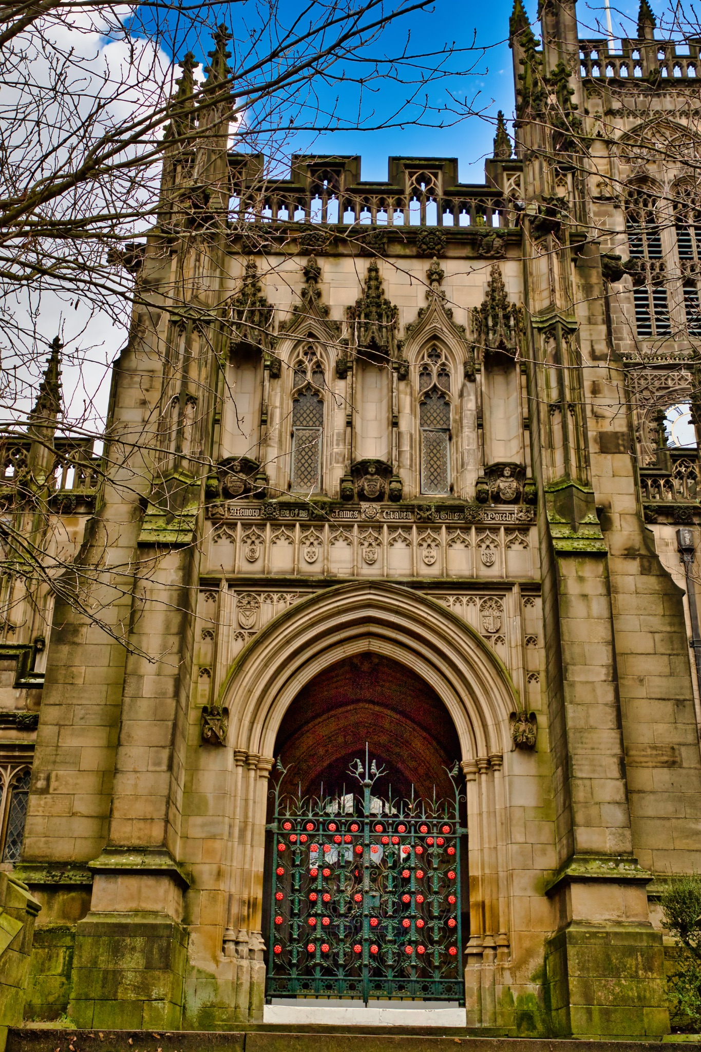 Sandstone Church Entrance with Ornate Carvings and Decorated Gate in Manchester, UK.
