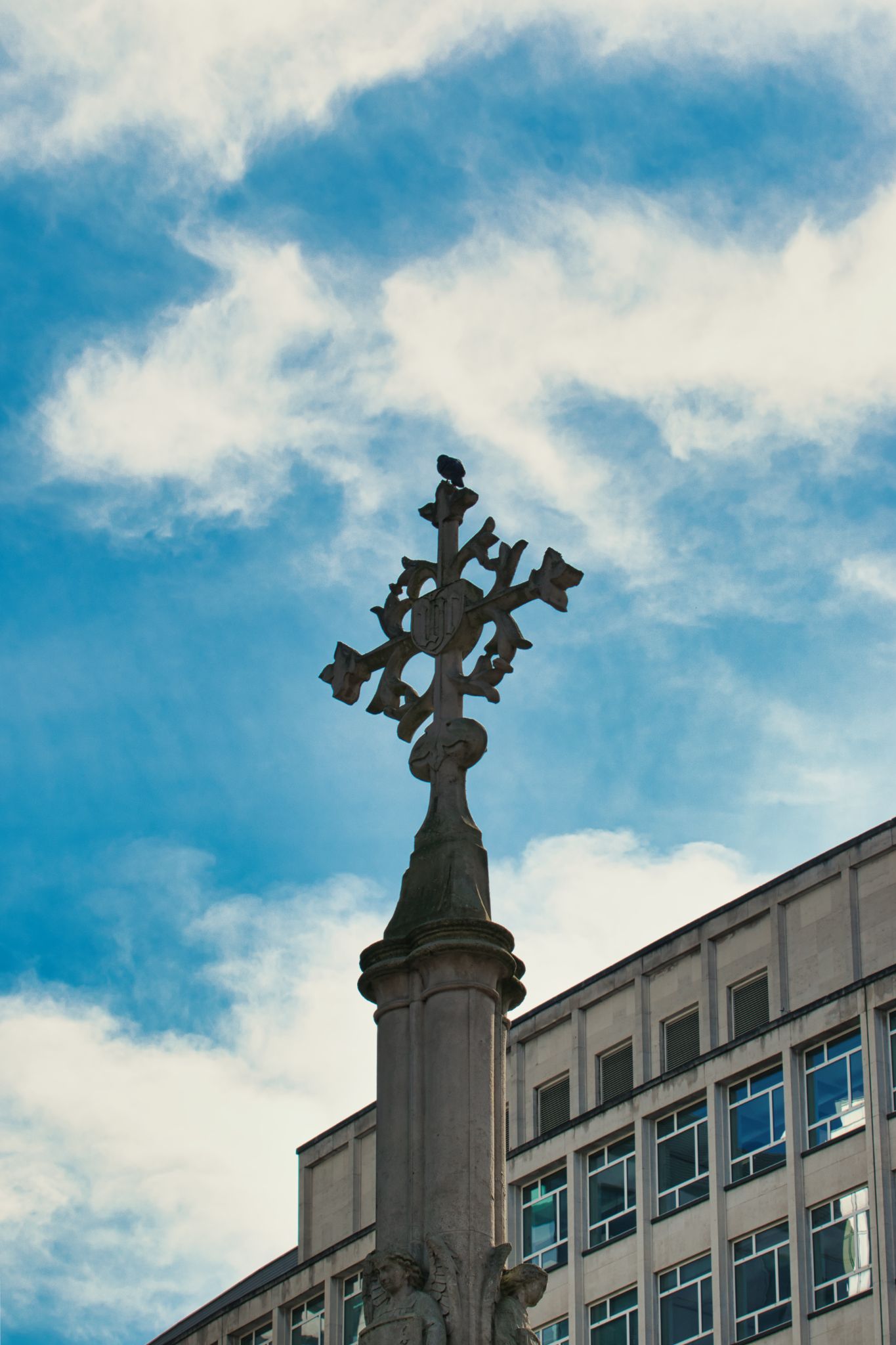 Stone Cross Monument With Bird and Building in Manchester, UK.