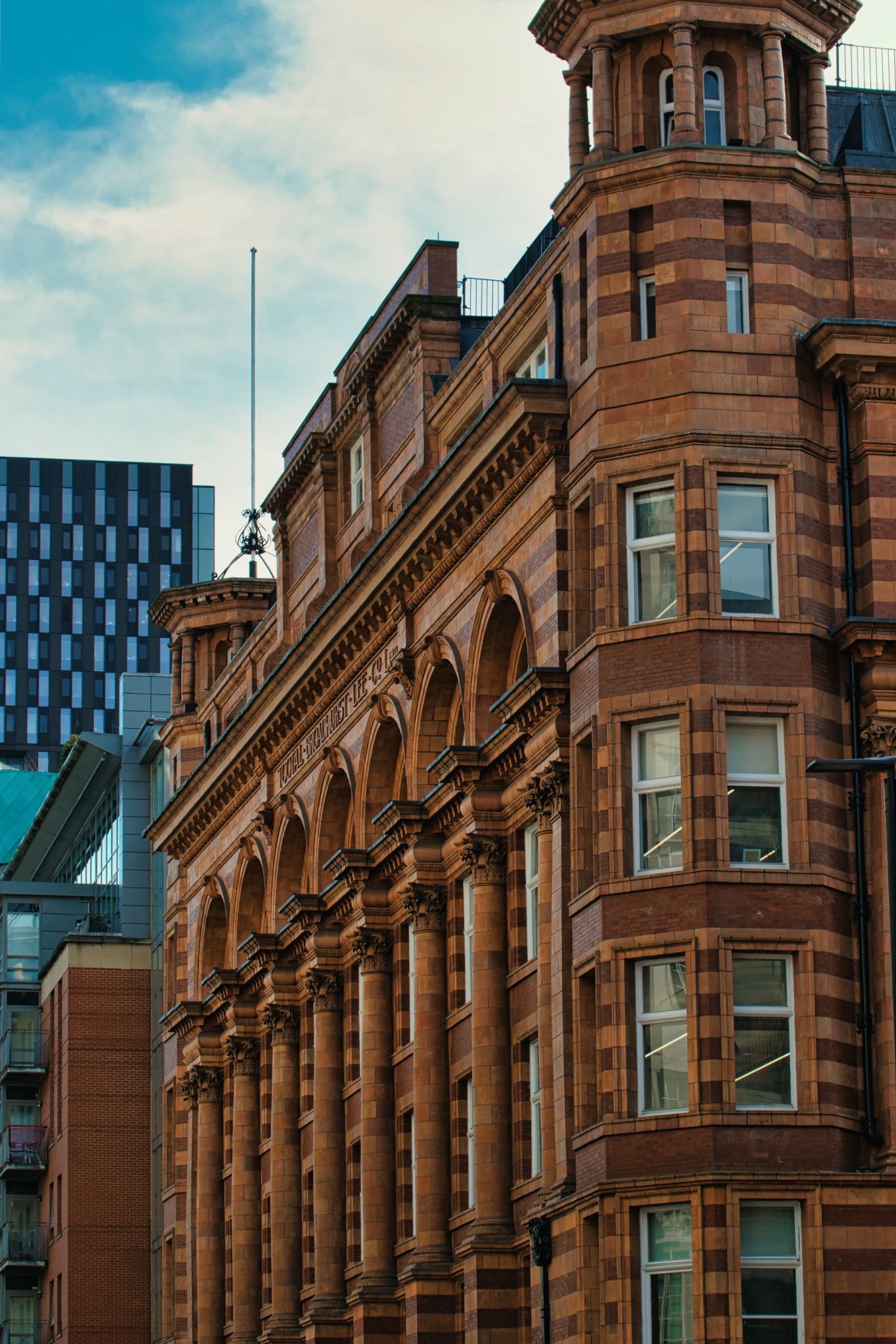 Brown Brick Building with Arches, Columns, and Modern Building in Manchester, UK.