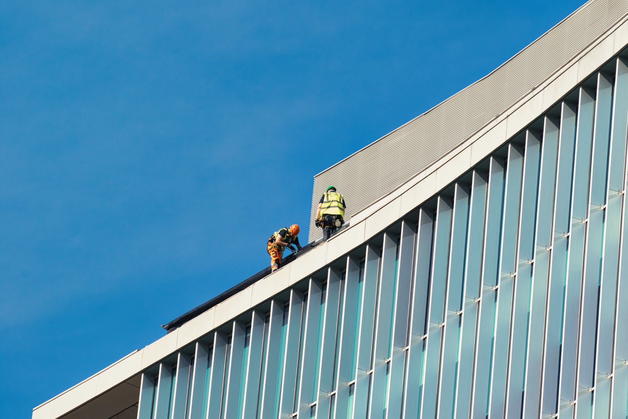 Workers on Roof of Modern Building with Glass Facade in Manchester, UK.