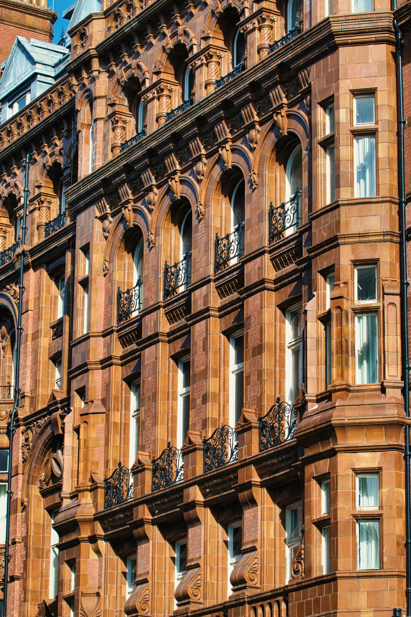 Brown Stone Building Facade with Arched Windows and Balconies in Manchester, UK.