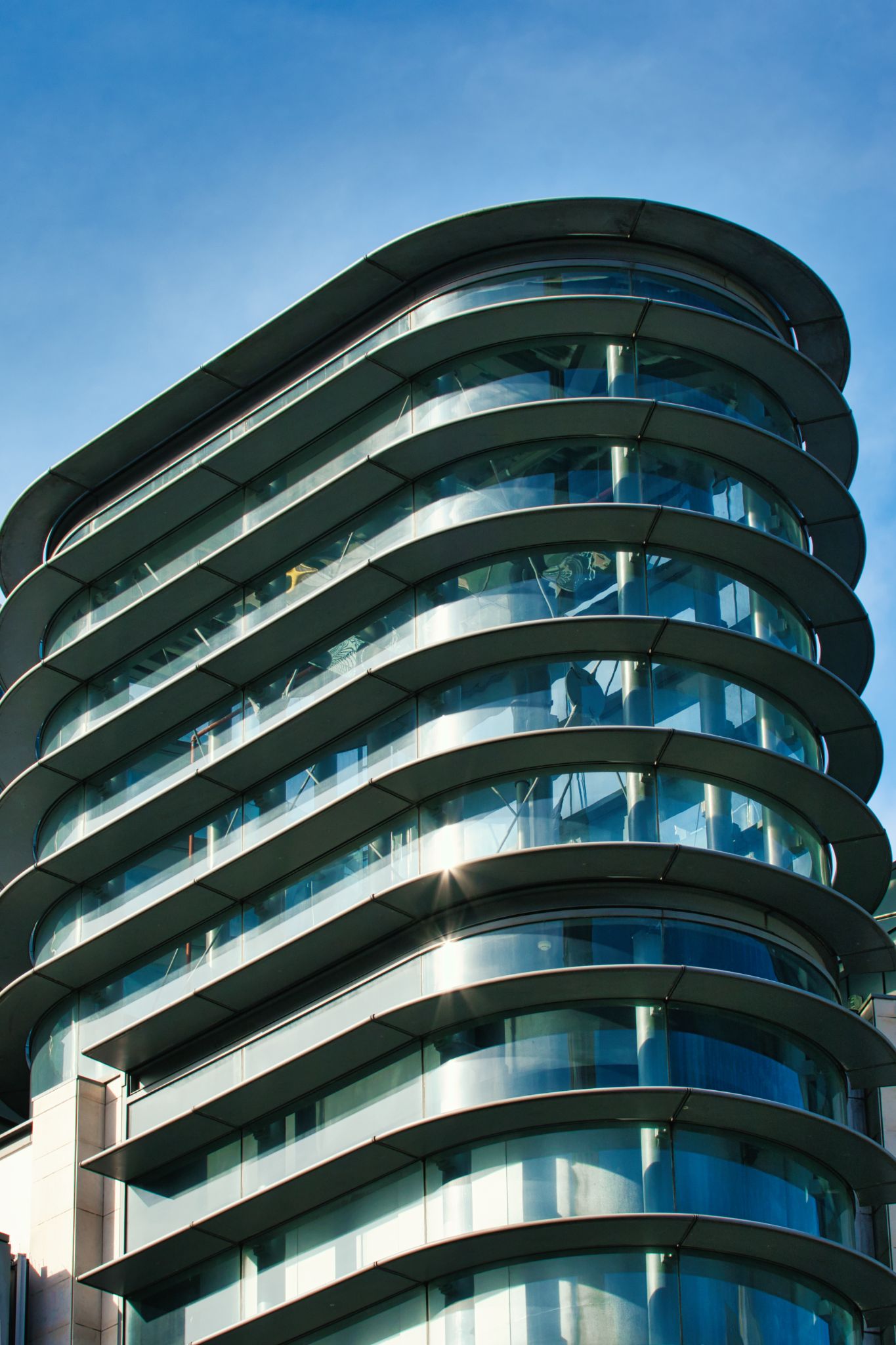 Curved Glass Building with Metal Framing Against Blue Sky in Manchester, UK.