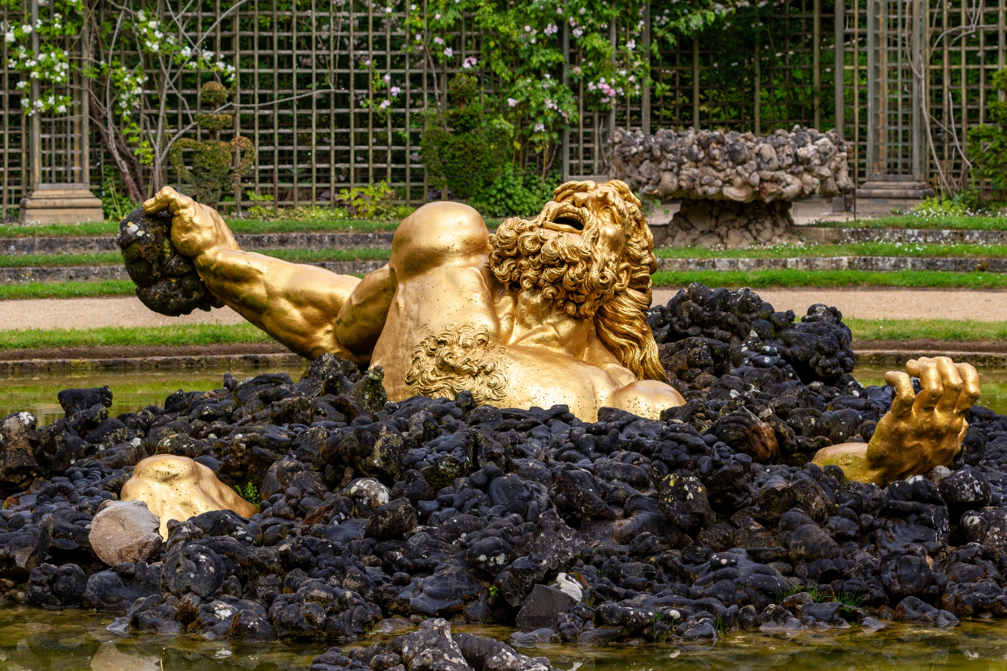 Gilded Statue Emerging from Rocks in Garden Pond at Versailles Gardens, Paris.