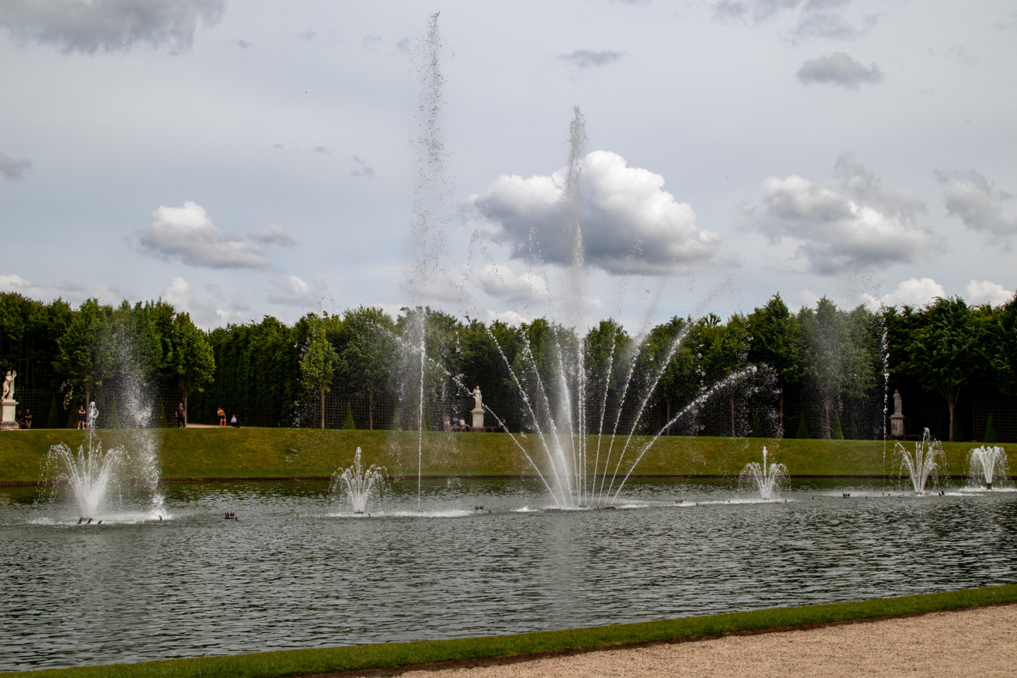 Multiple Fountains in Pond with Greenery and Cloudy Sky at Palace of Versailles, Paris.