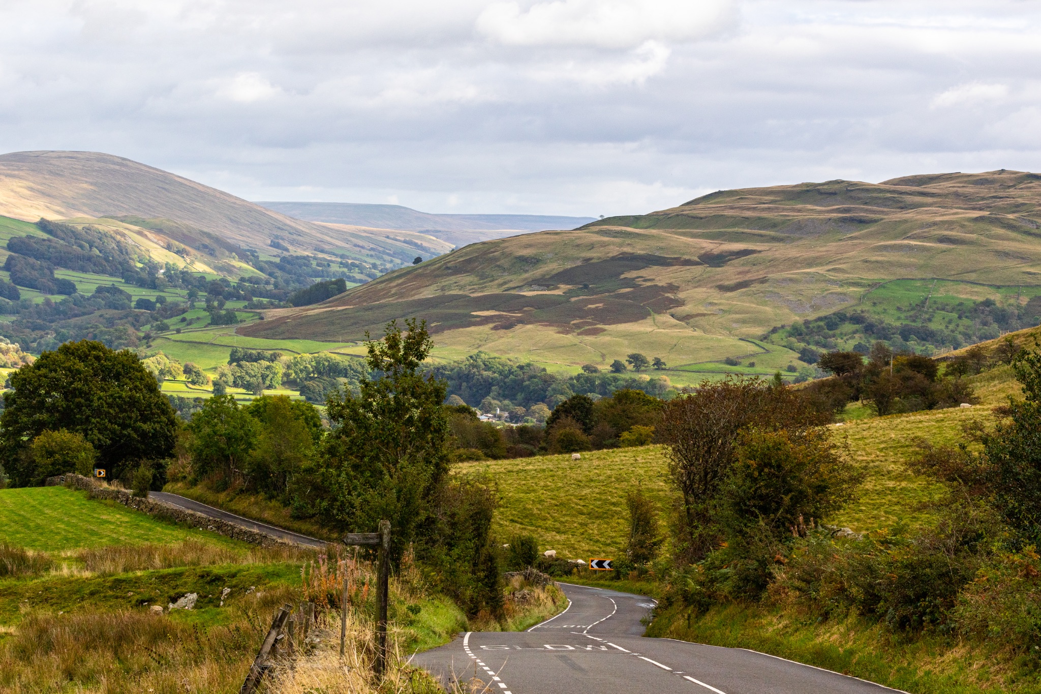 Scenic view of a winding road through lush green hills under a cloudy sky.