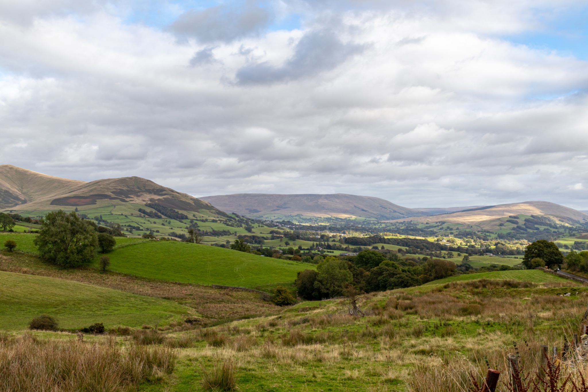 Scenic view of rolling hills with lush greenery under a cloudy sky.