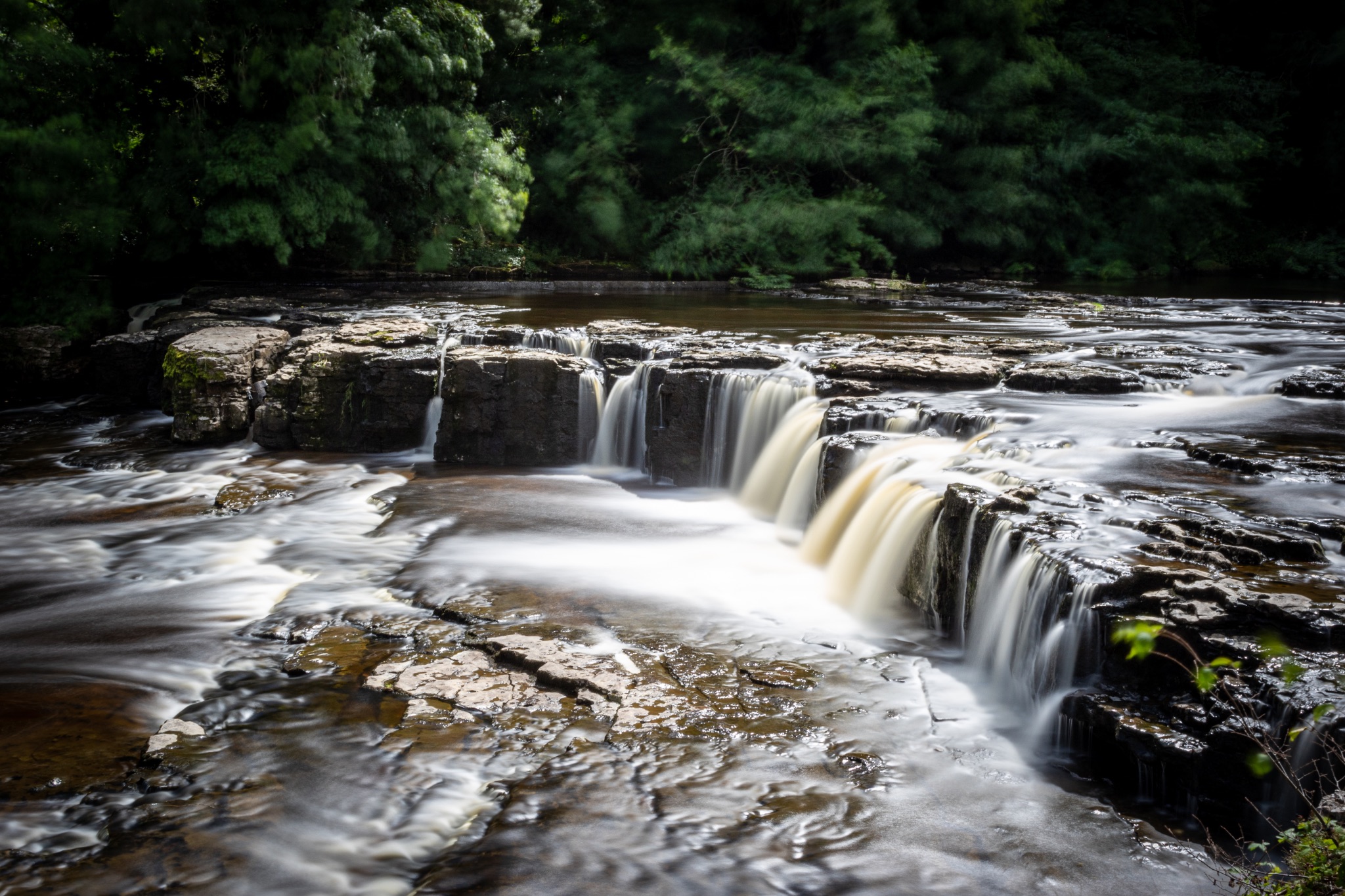 Serene waterfall with smooth flowing water in a lush forest setting.