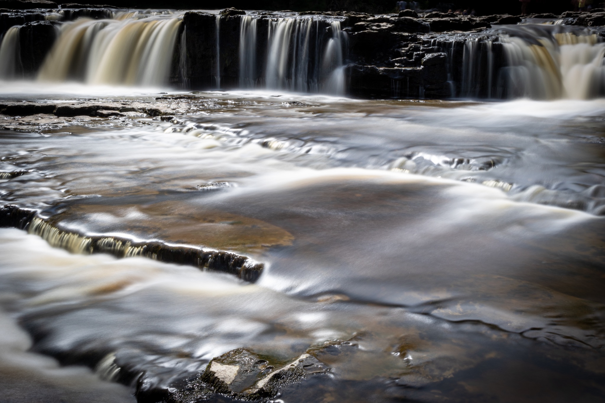 Serene cascading waterfall over smooth rocks with a silky water effect, conveying tranquility and the beauty of nature.